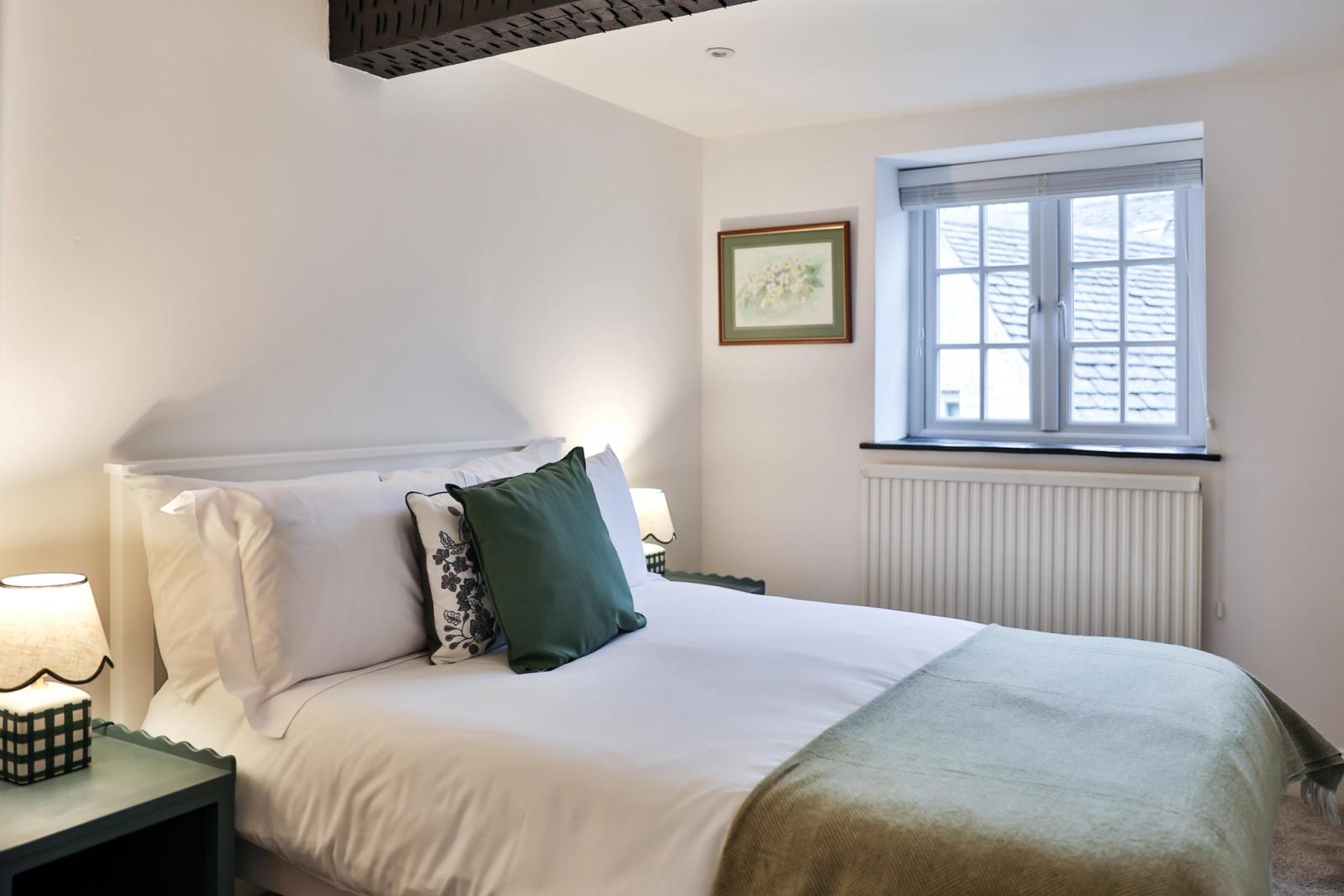 Master bedroom with white bed, green cushions, windows, and cream walls
