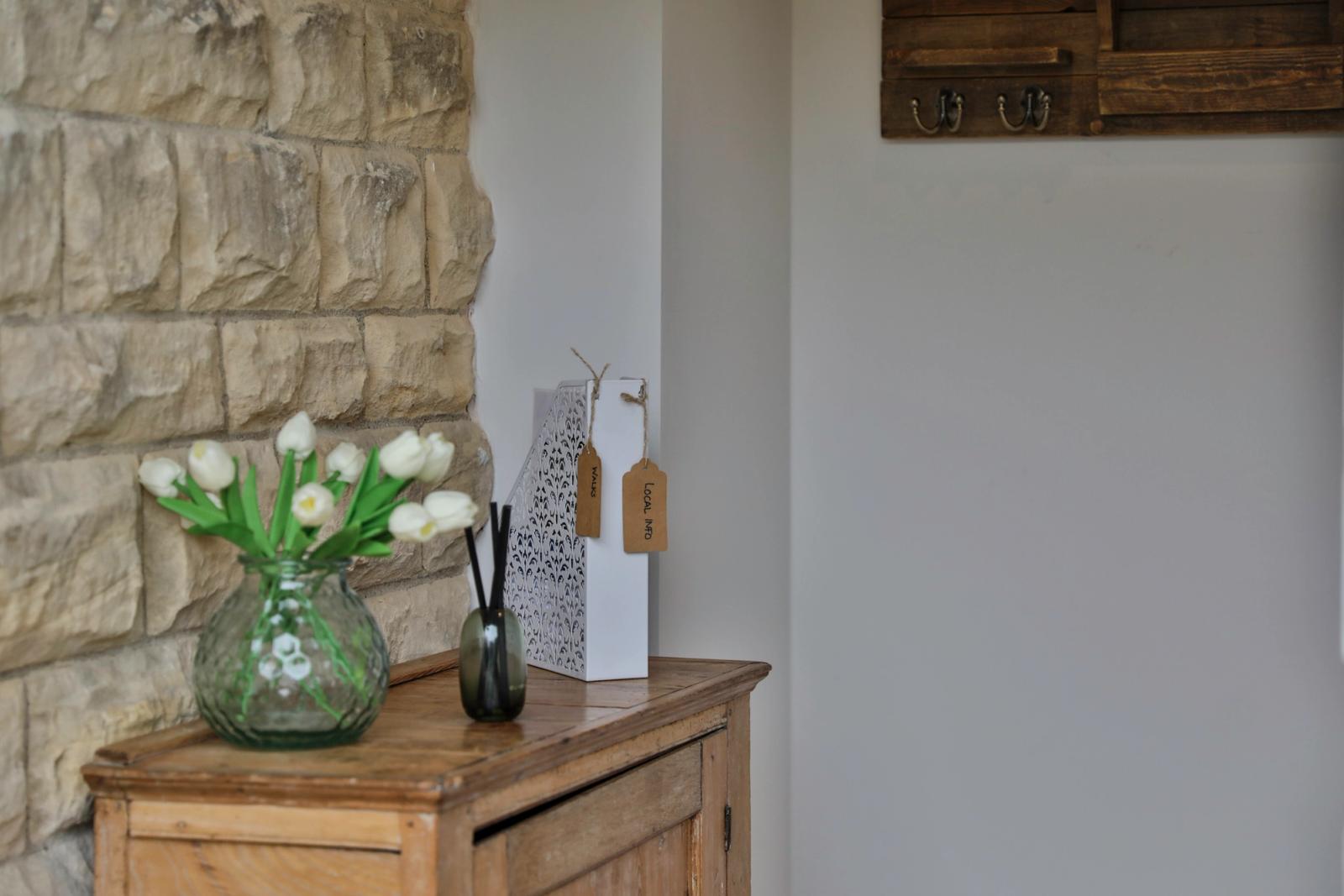 Entryway with stone walls, wooden shelf, green flowers in vase, storage items, simple décor