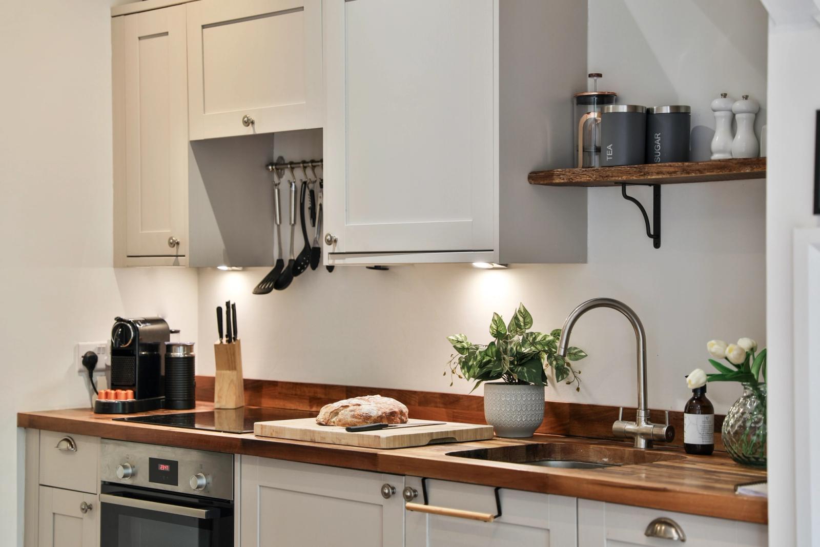 Compact kitchen with cream cabinets, black oven, wooden countertop, open shelving, sink window