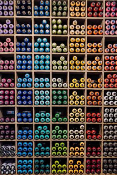 a shelf filled with lots of different colored spray paint cans .