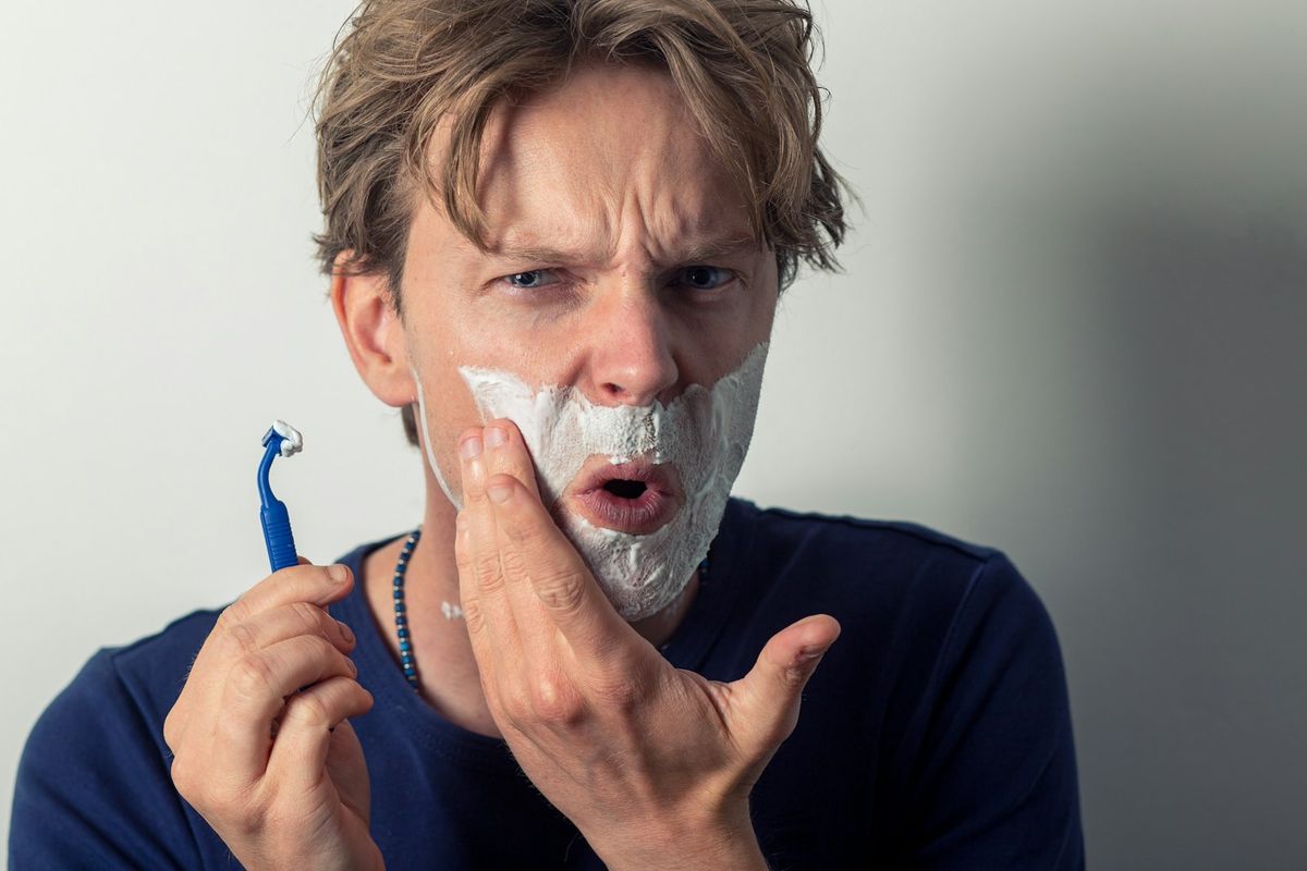 A man working beard balm through his beard with both hands in front of a bathroom mirror