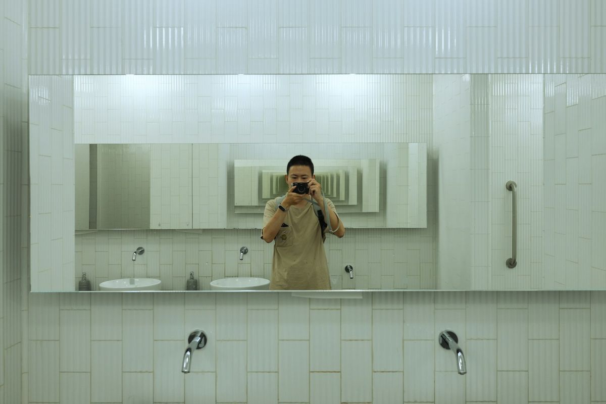 A man setting his beard with a comb in front of a bathroom mirror during his morning routine