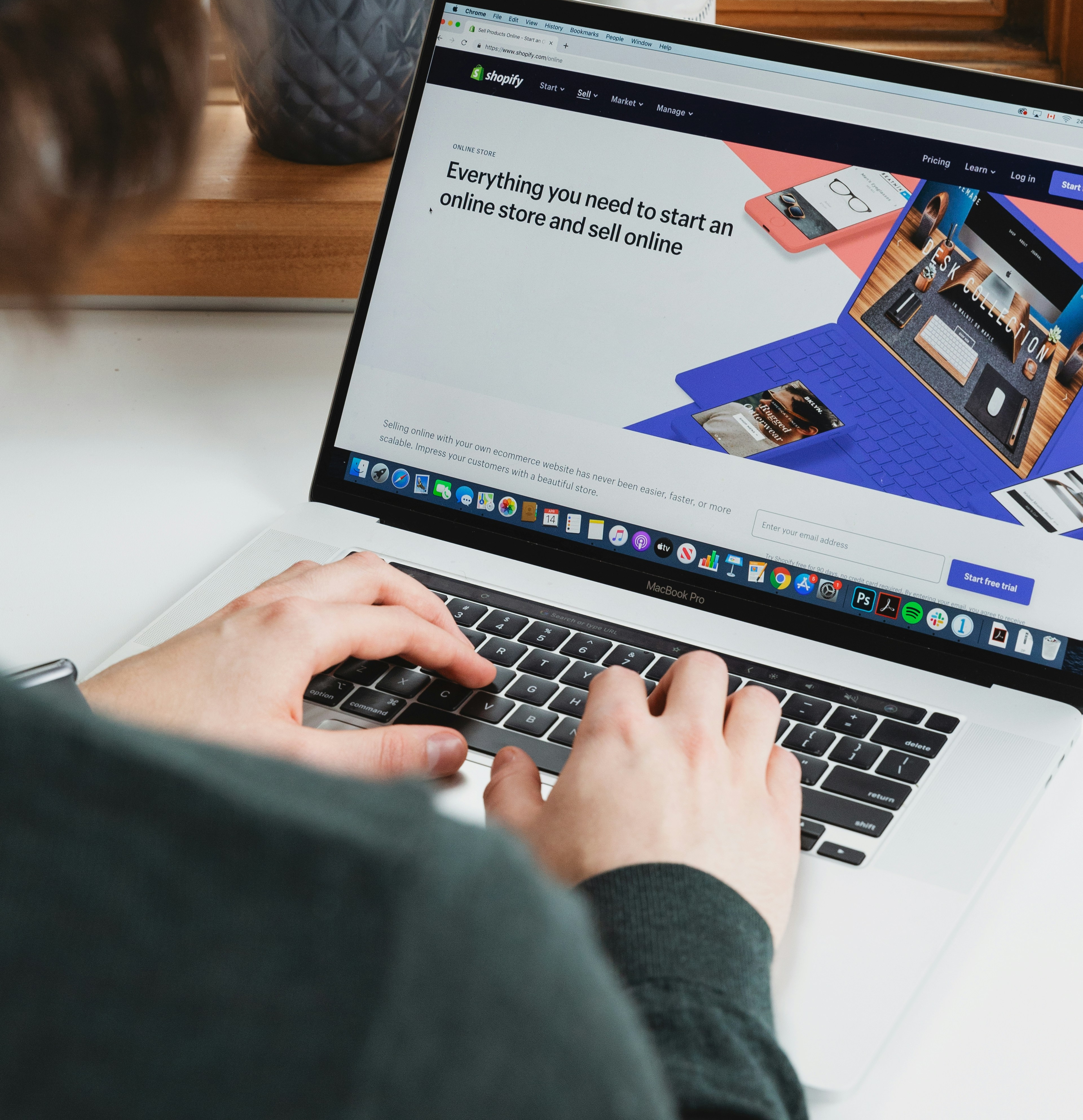Person typing on a laptop showing the Shopify website homepage for creating an online store.