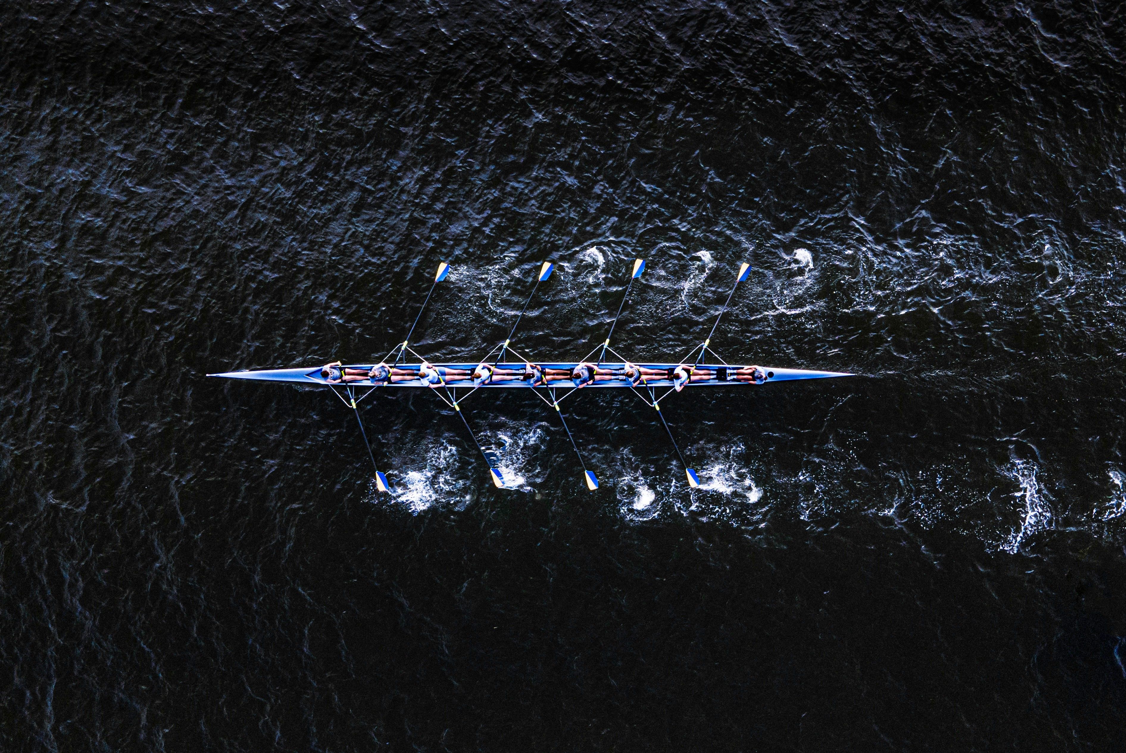 Overhead view of a rowing crew synchronizing their strokes on dark water