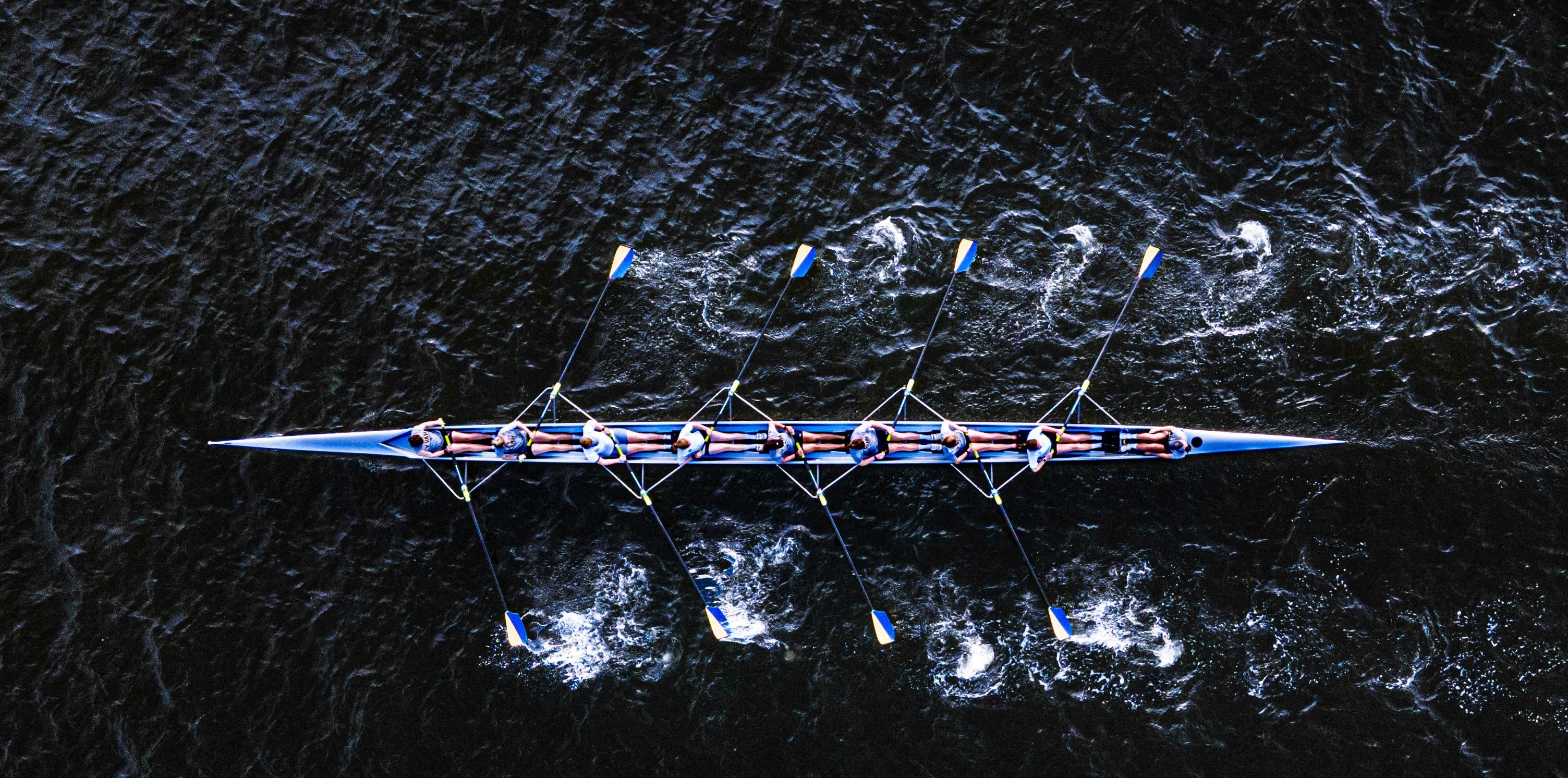 Overhead view of a rowing crew synchronizing their strokes on dark water