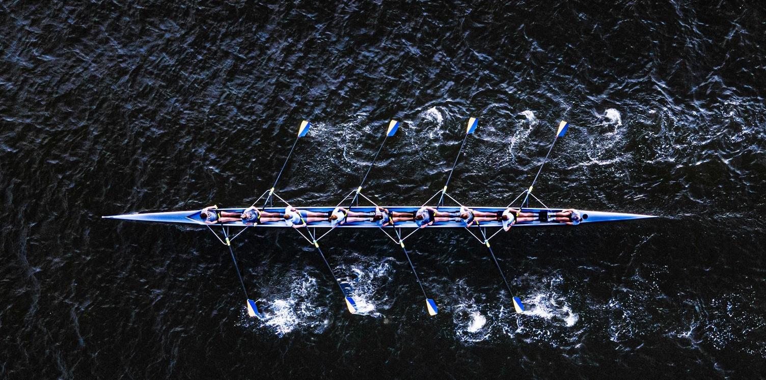 Overhead view of a rowing crew synchronizing their strokes on dark water