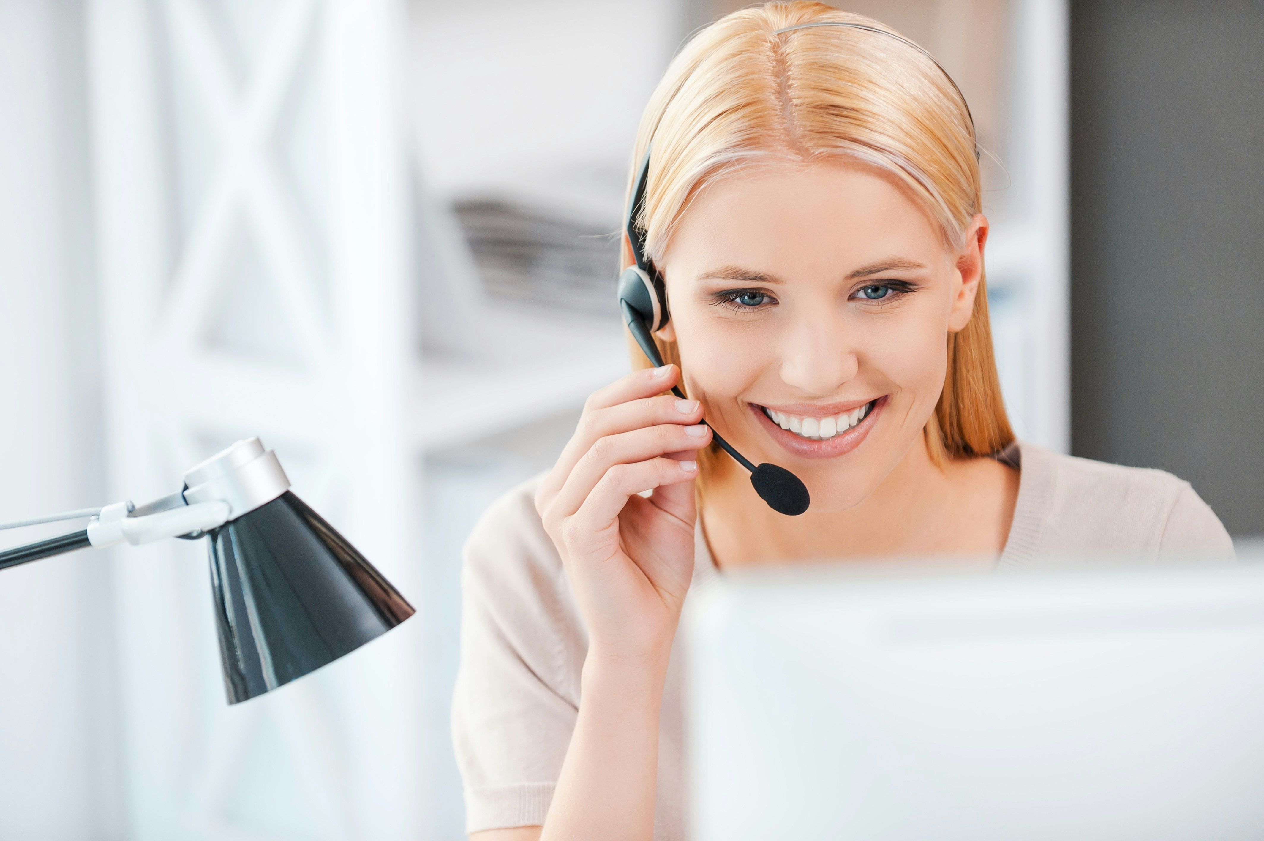 Smiling woman wearing a headset while working on a computer, representing customer support and consultation.