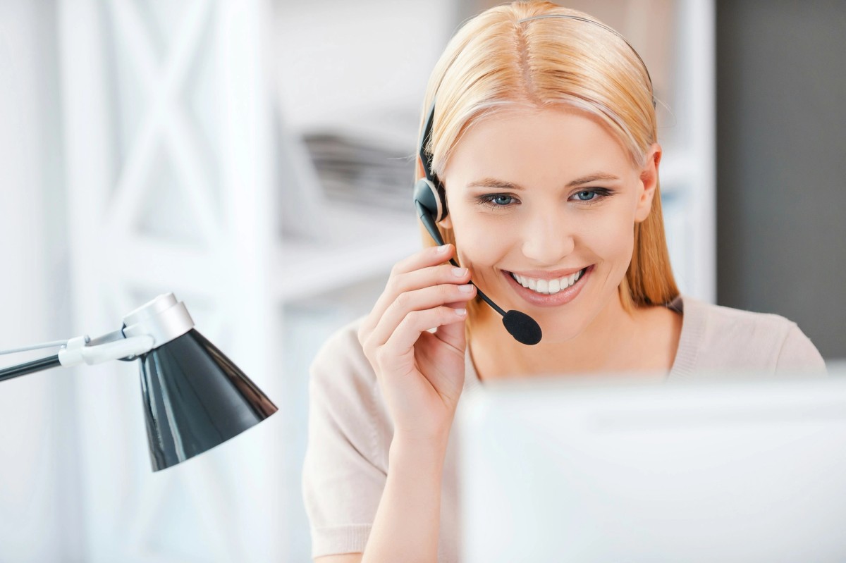 Smiling woman wearing a headset while working on a computer, representing customer support and consultation.