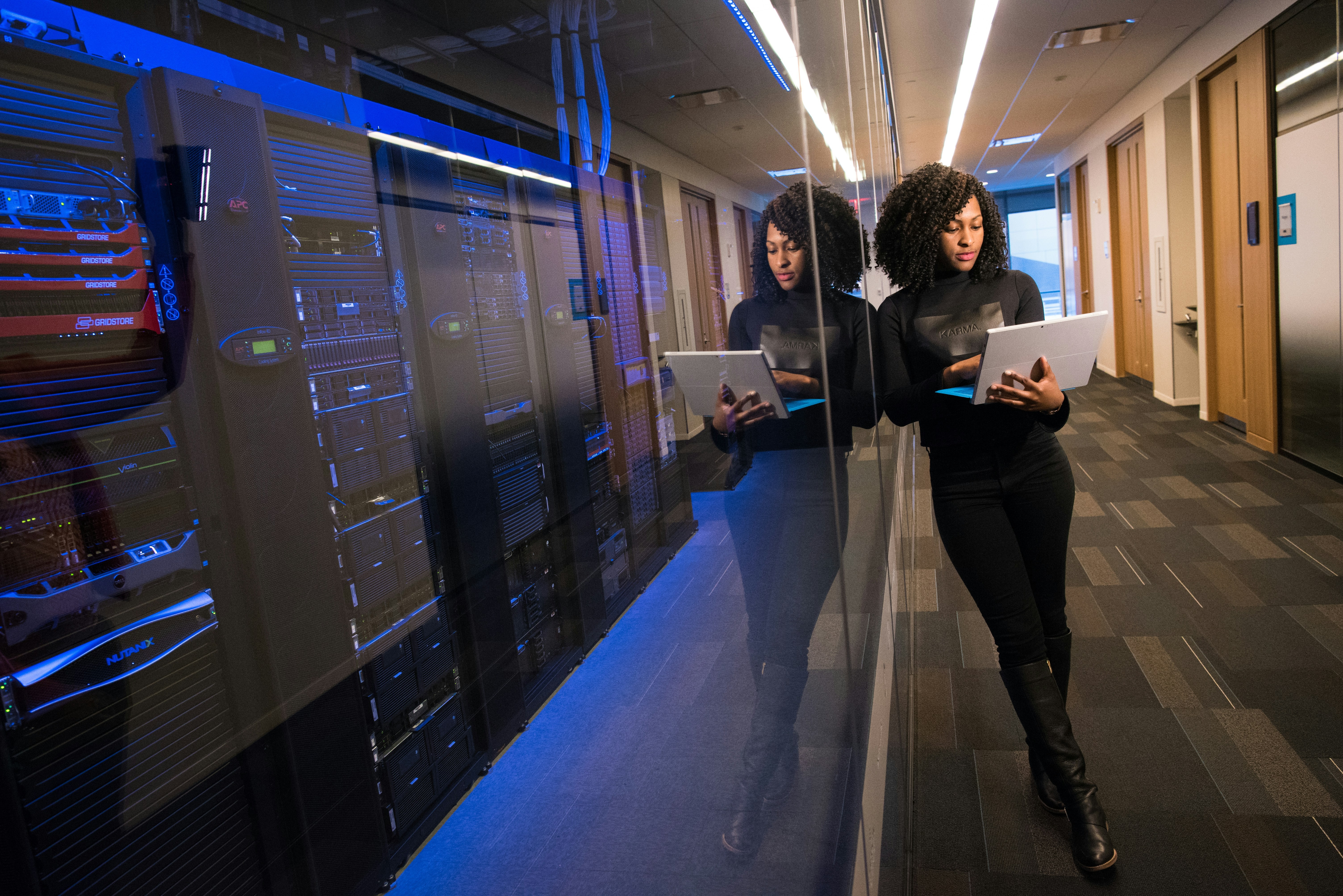 Woman with laptop standing in a data center hallway with server racks