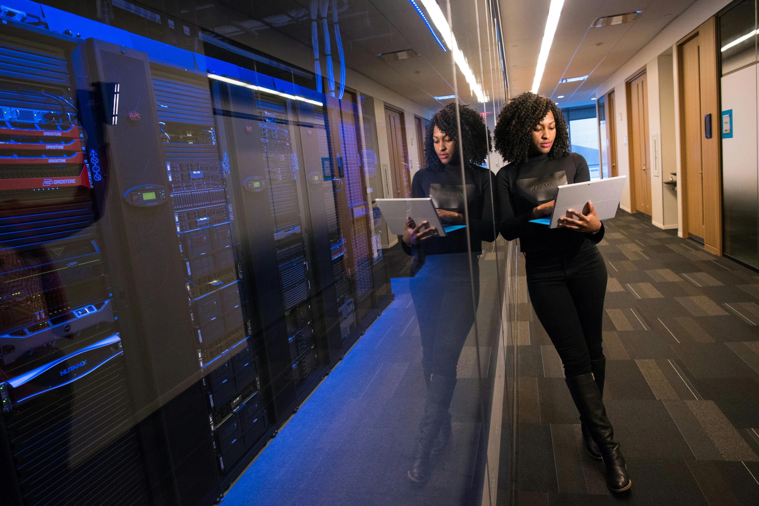 Woman with laptop standing in a data center hallway with server racks