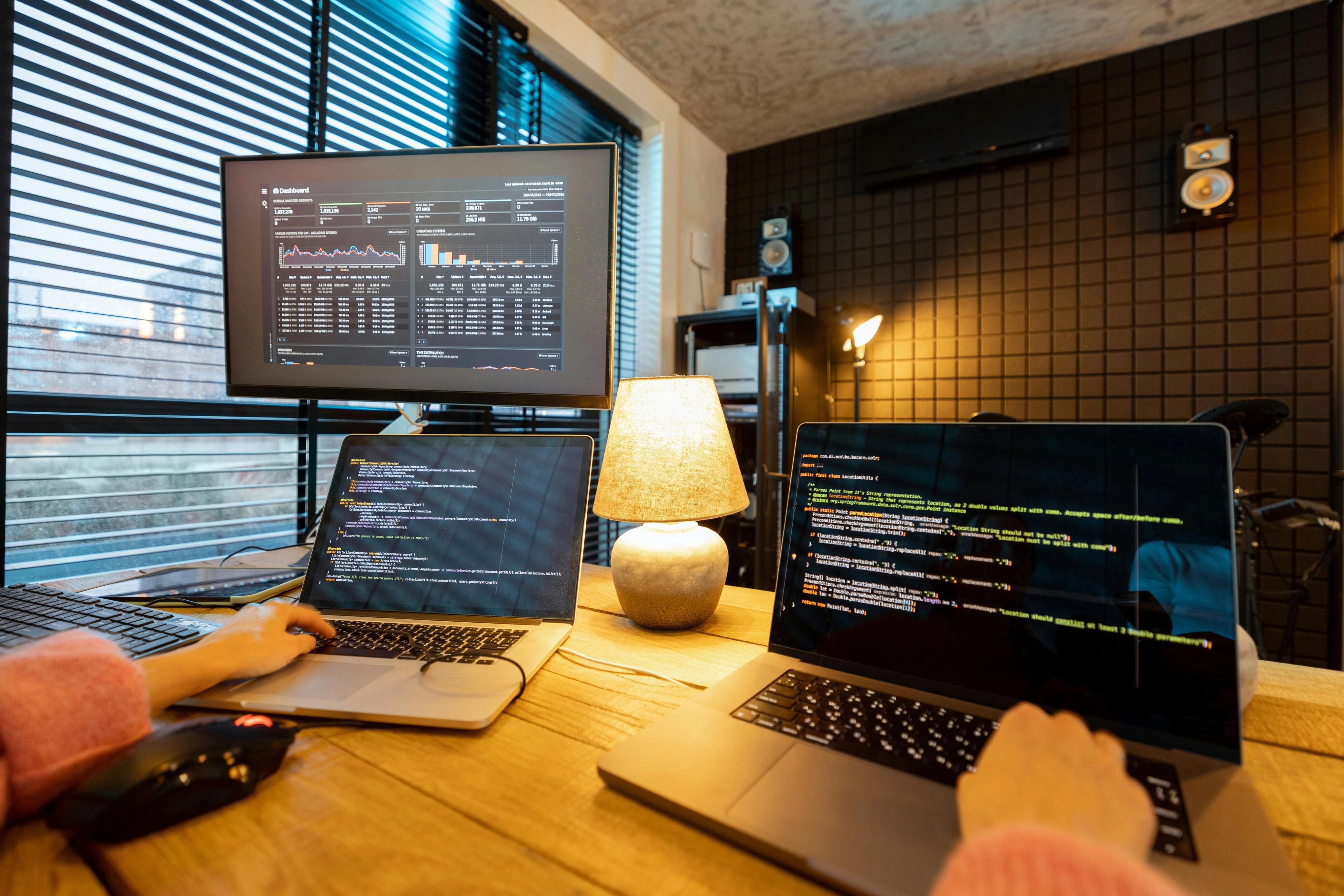 Developer writing code on a laptop with multiple monitors displaying programming scripts in a modern workspace.