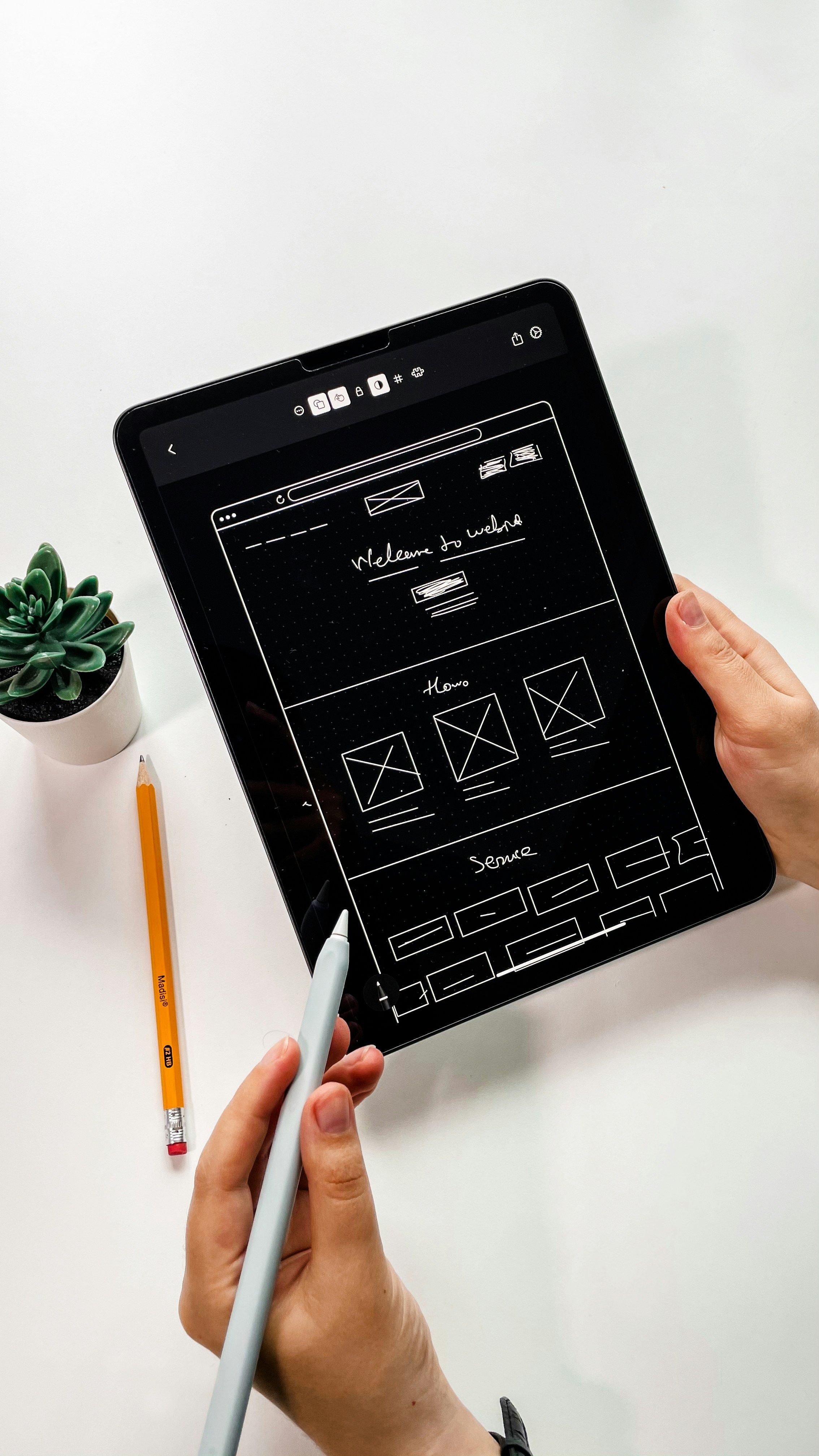 Hand holding a tablet with a website wireframe design, representing UI/UX prototyping and user interface planning.