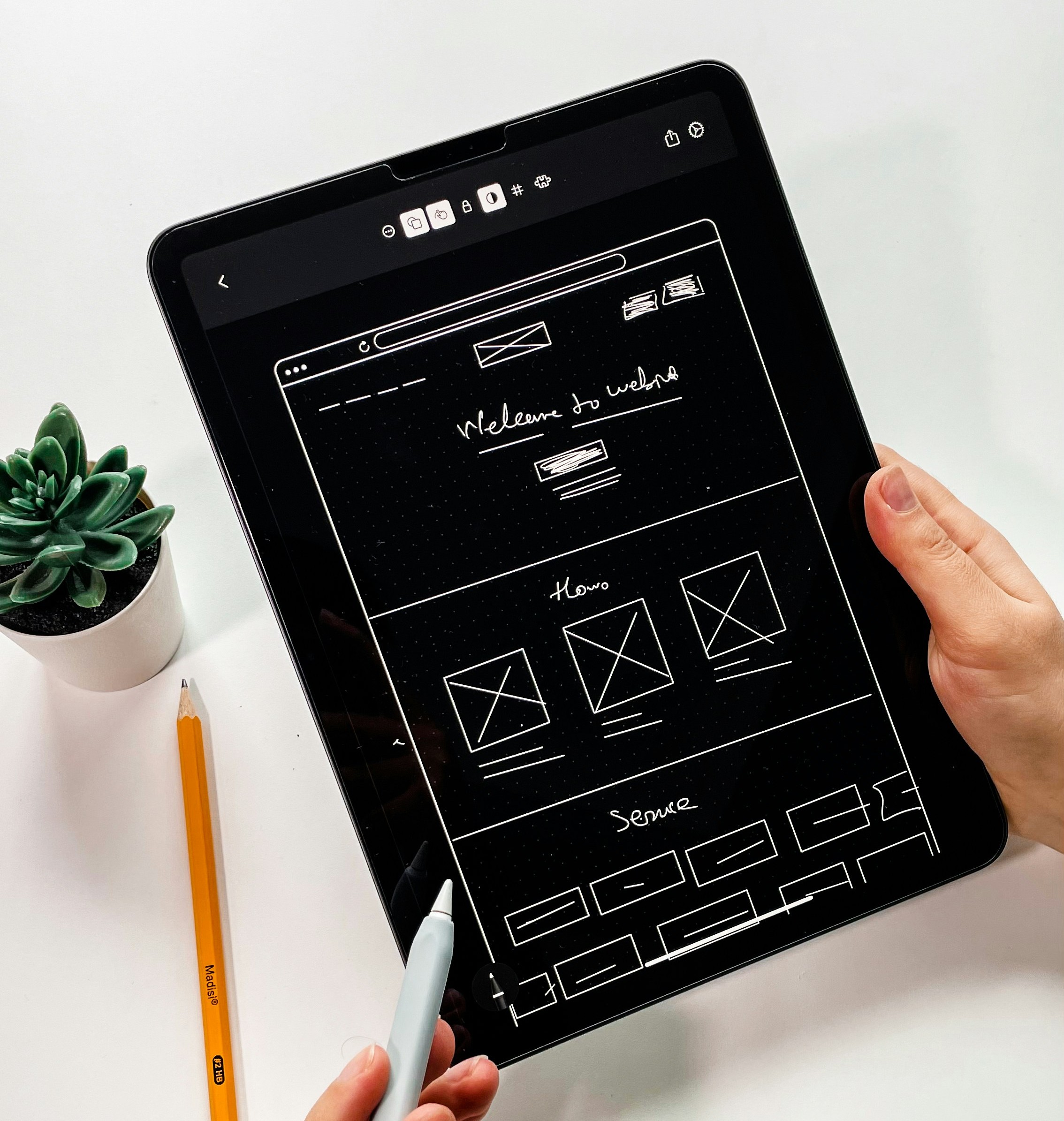 Hand holding a tablet with a website wireframe design, representing UI/UX prototyping and user interface planning.
