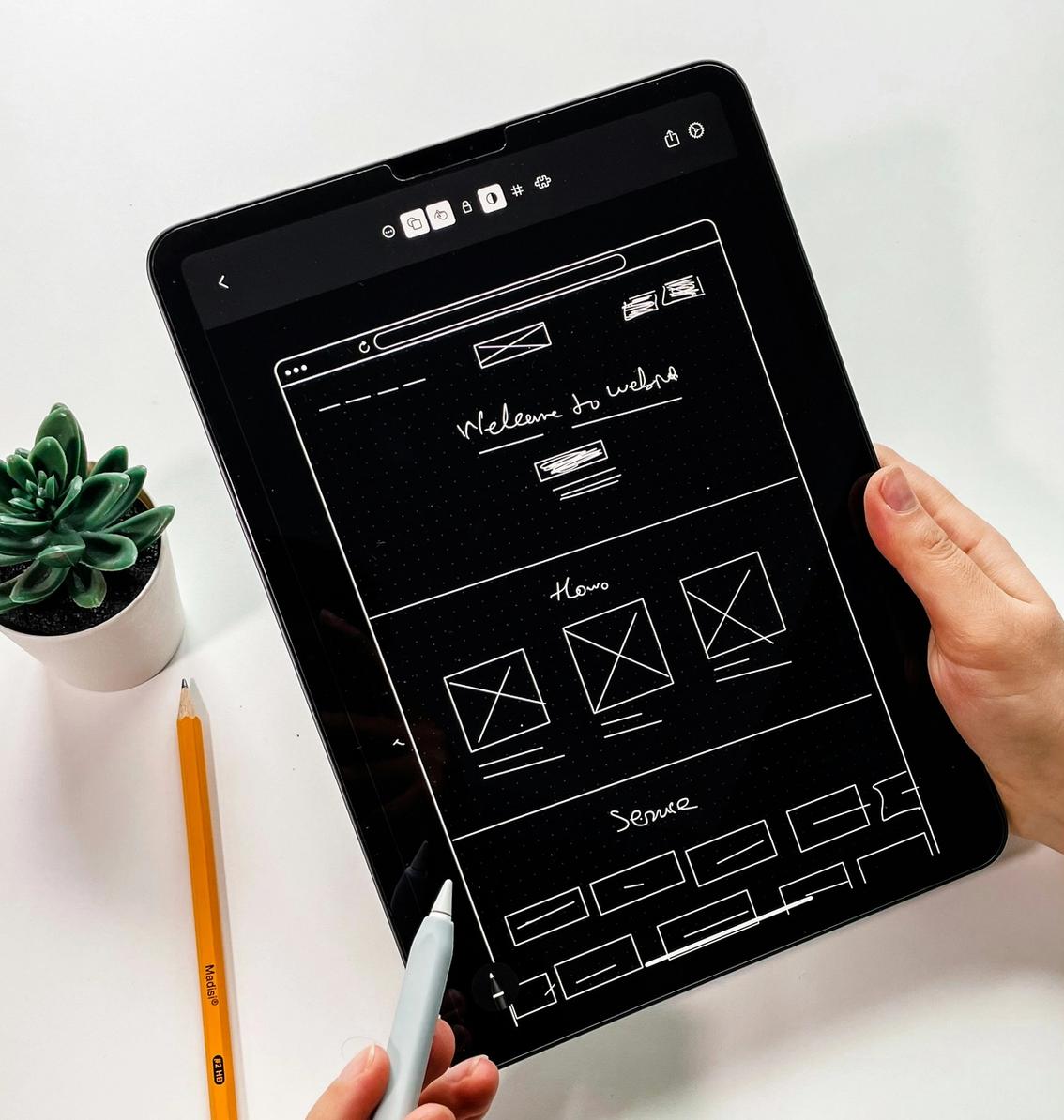 Hand holding a tablet with a website wireframe design, representing UI/UX prototyping and user interface planning.