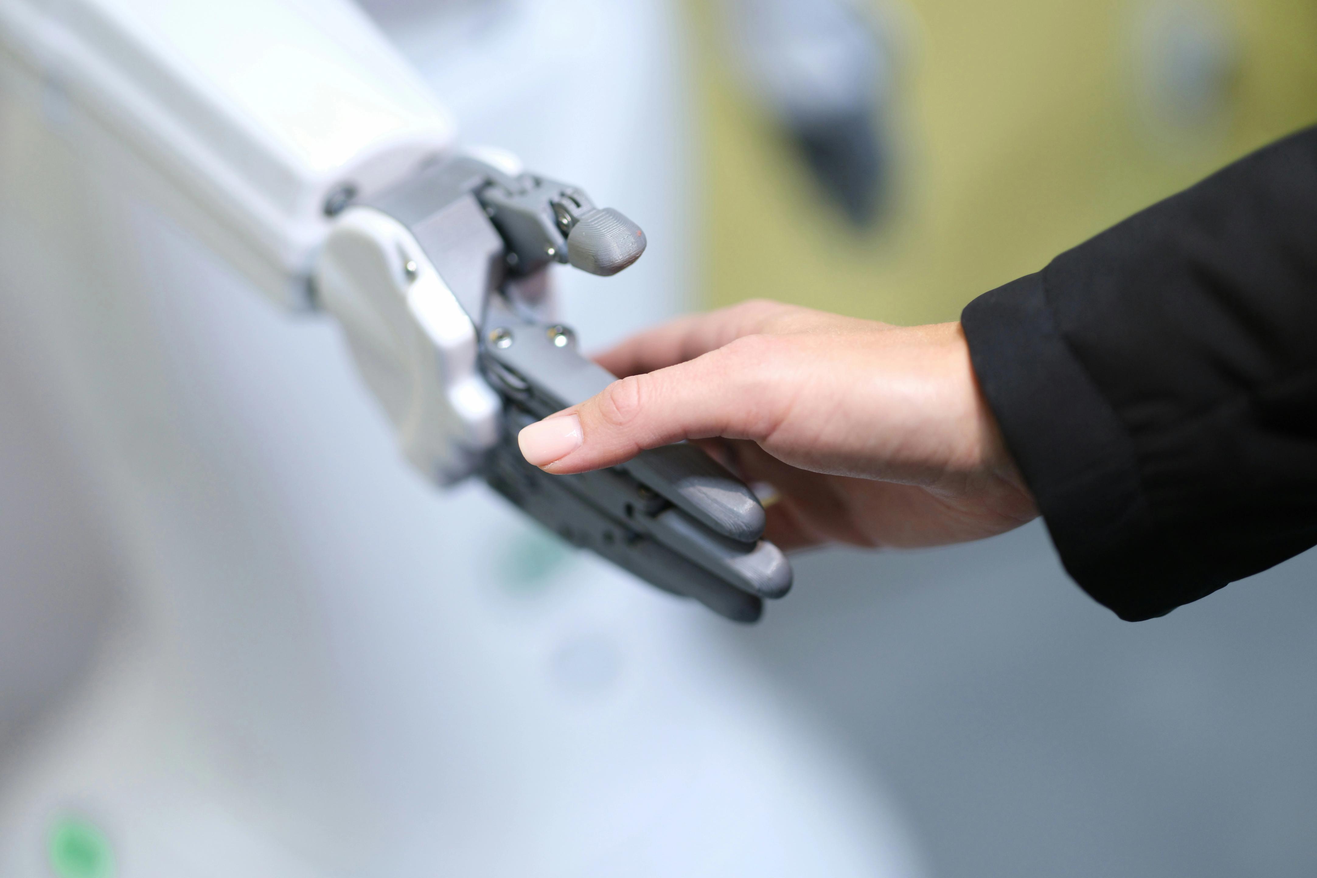 Human hand shaking hands with a robotic hand in a collaboration gesture.