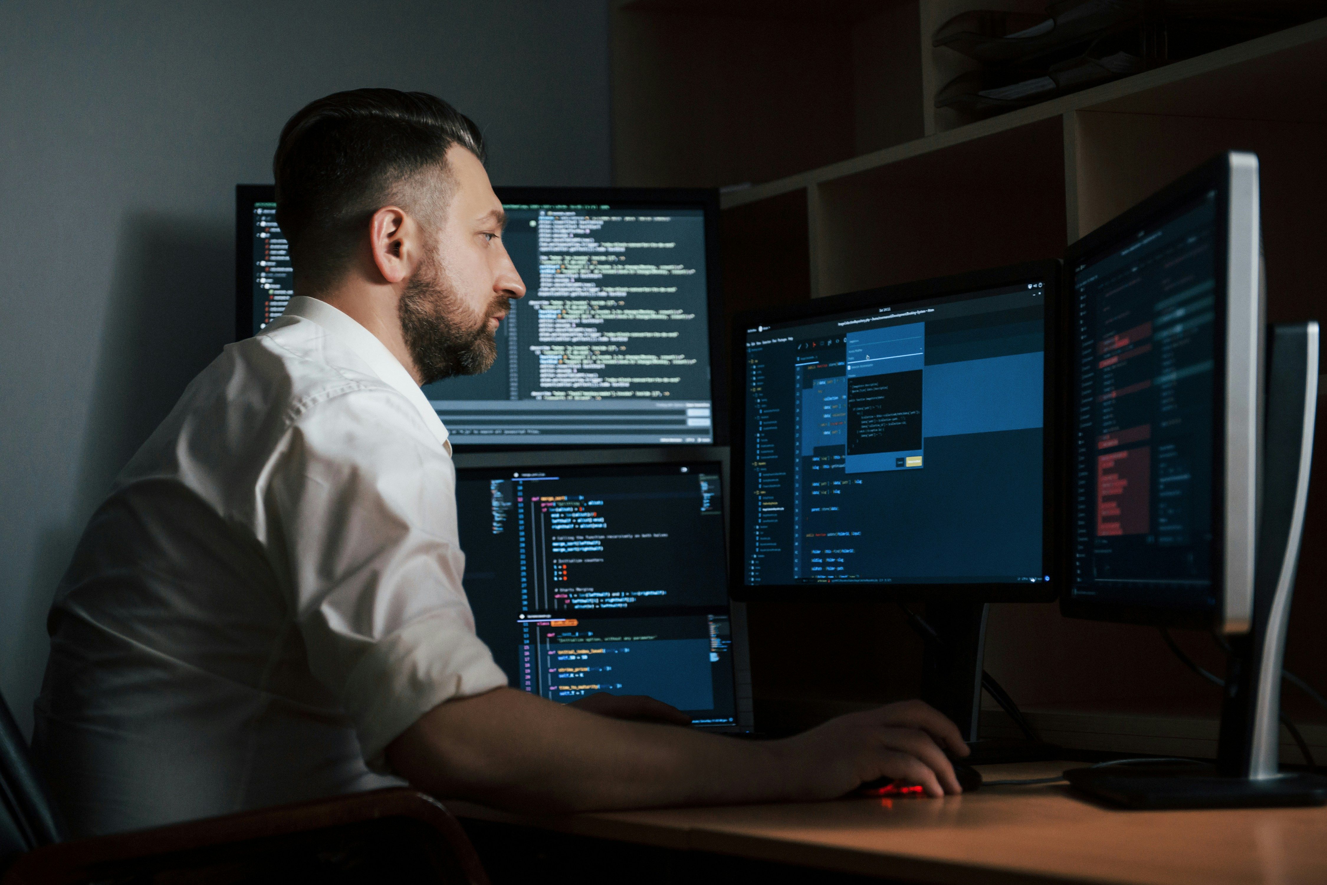 Software developer working on multiple monitors with code displayed, representing custom web development services.