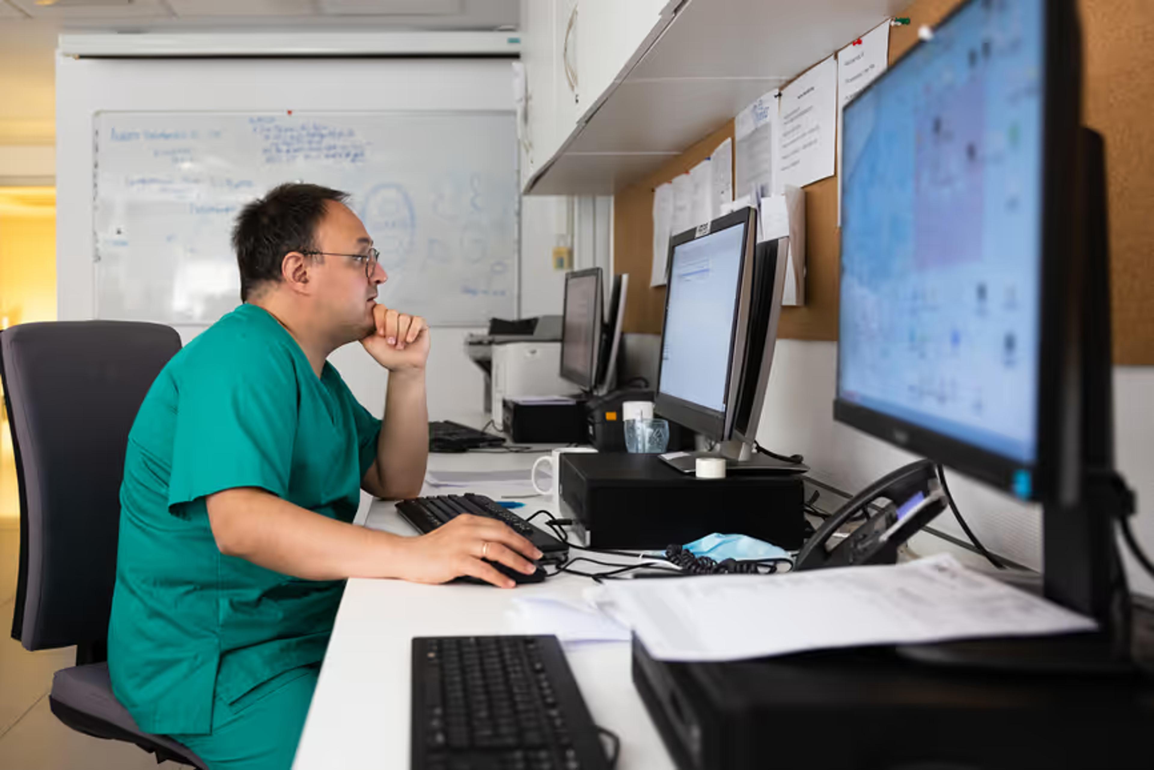 A clinician works at a desk with several monitors