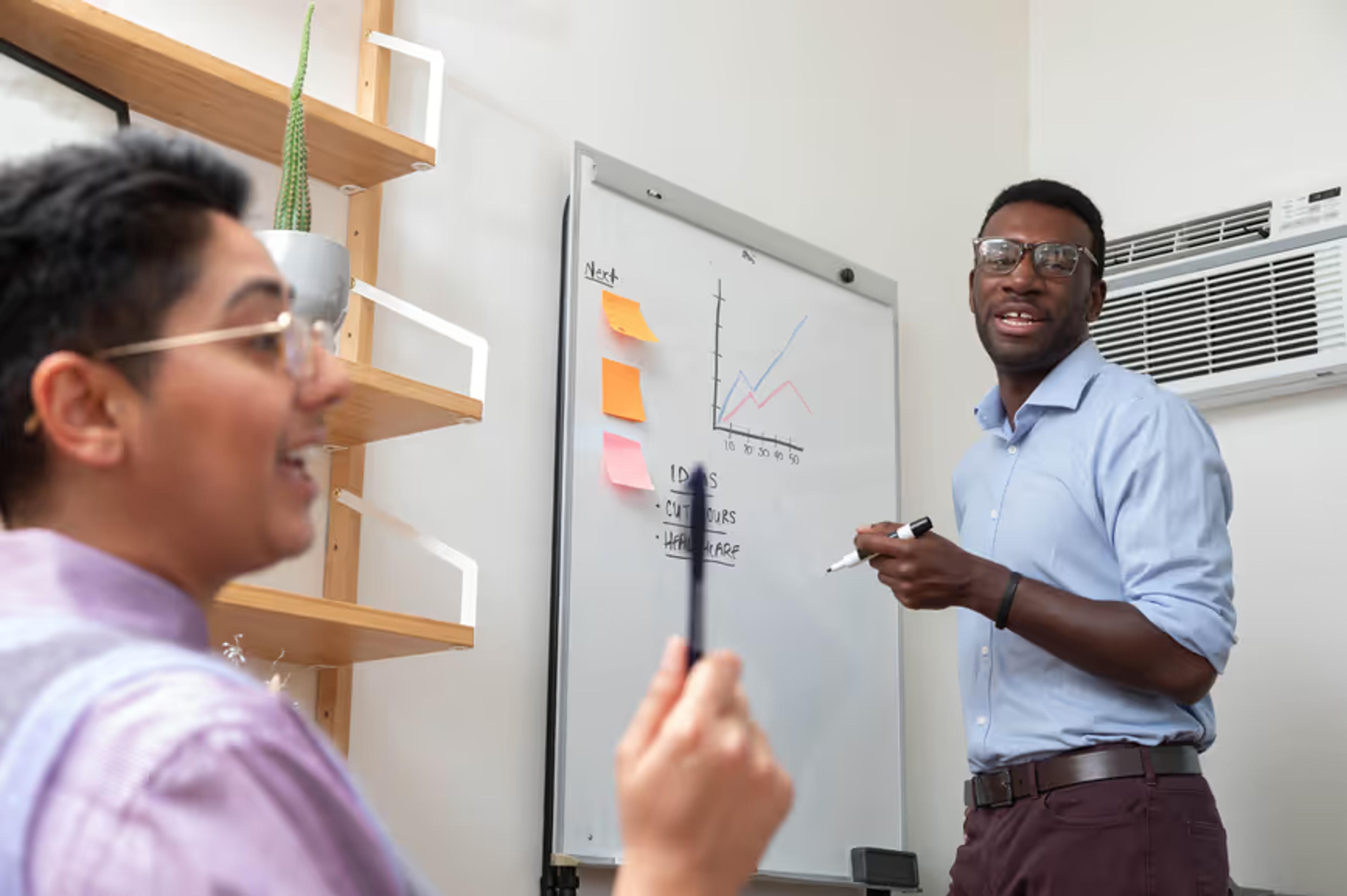 Two colleagues discuss notes at a whiteboard