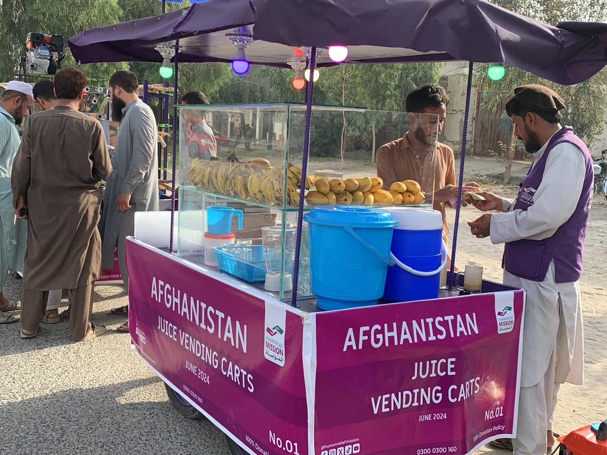Afghan man with his Fresh Juice cart (IGP) with Human Relief Mission aid worker buying juice