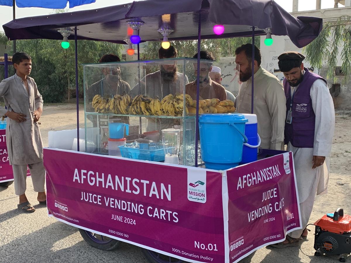 Afghan man with his Fresh Juice cart (IGP) with people buying from him