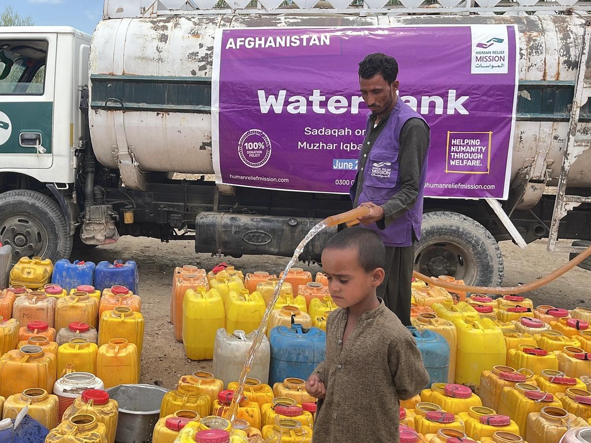 Child and HRM aid worker in Afghanistan pouring water into buckets from a Water tanker | Human Relief Mission