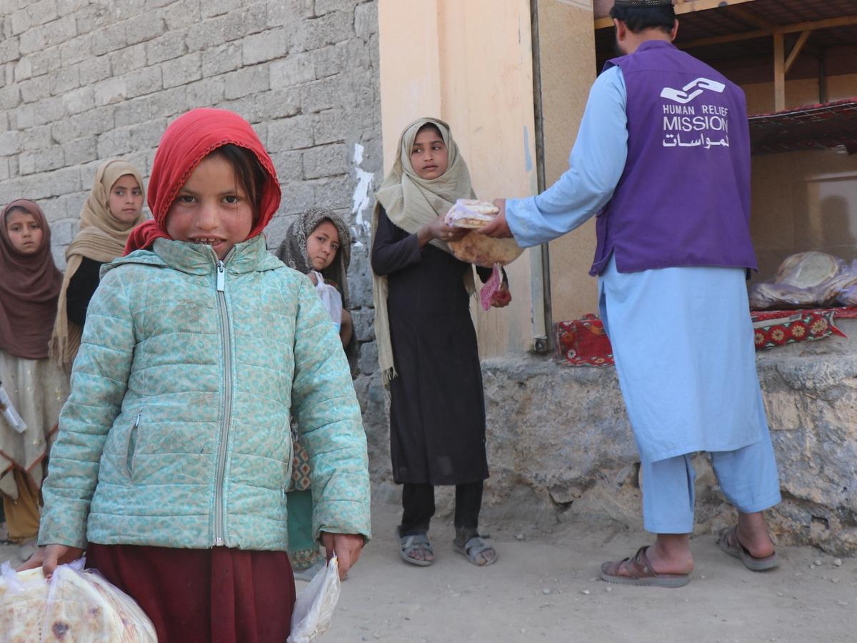 Child with a packet of bread and HRM Charity Aid Worker giving bread to Afghan girls | Human Relief Mission