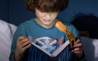 A child using the Flexilight book light for kids to read a book at night