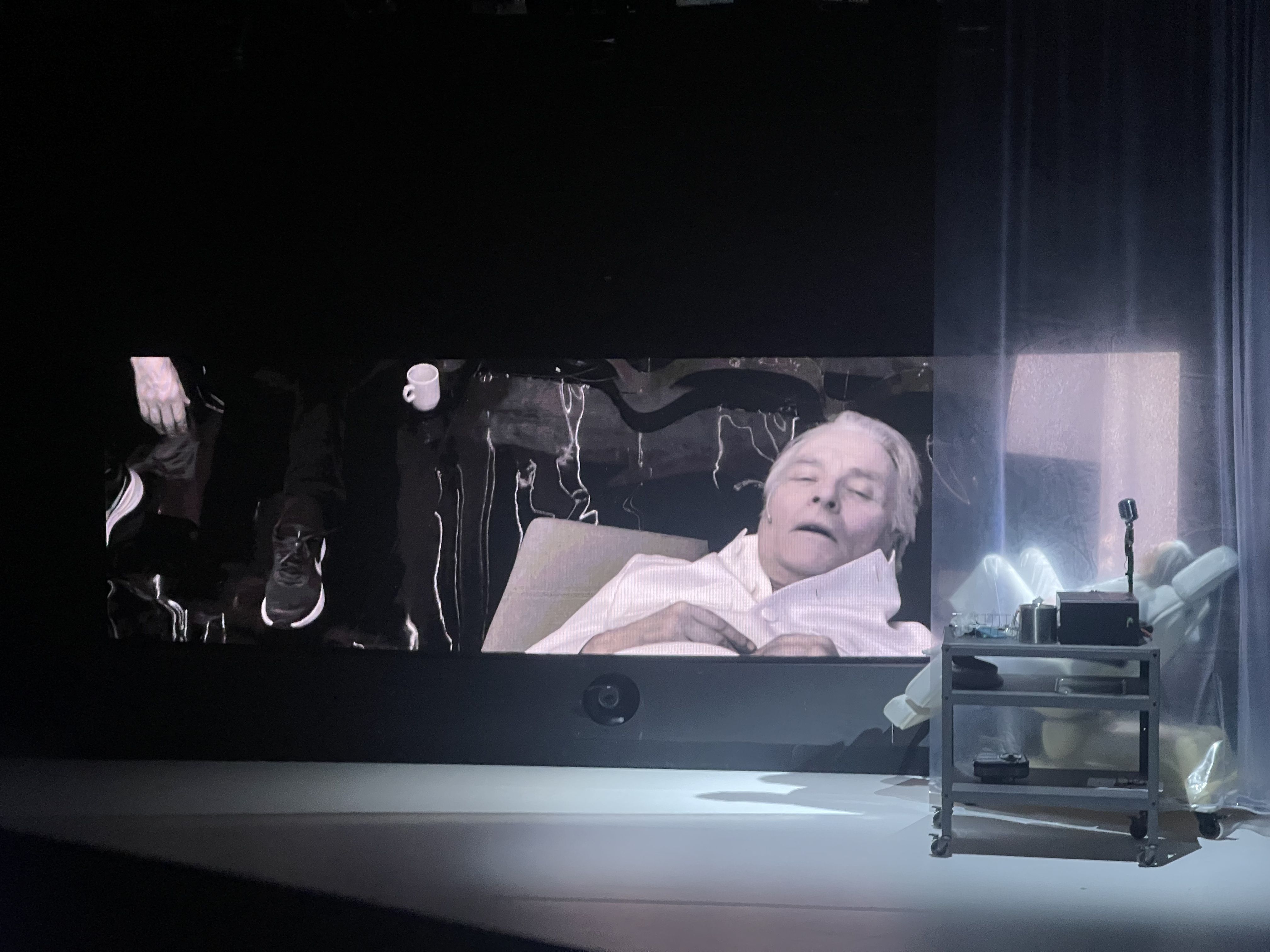 Prøvebilder fra scenen til forestillingen Kallocain - vi ser en mann som ligger i en tannlegelignende stol. Vi ser fjeset hans på en stor skjerm bak.