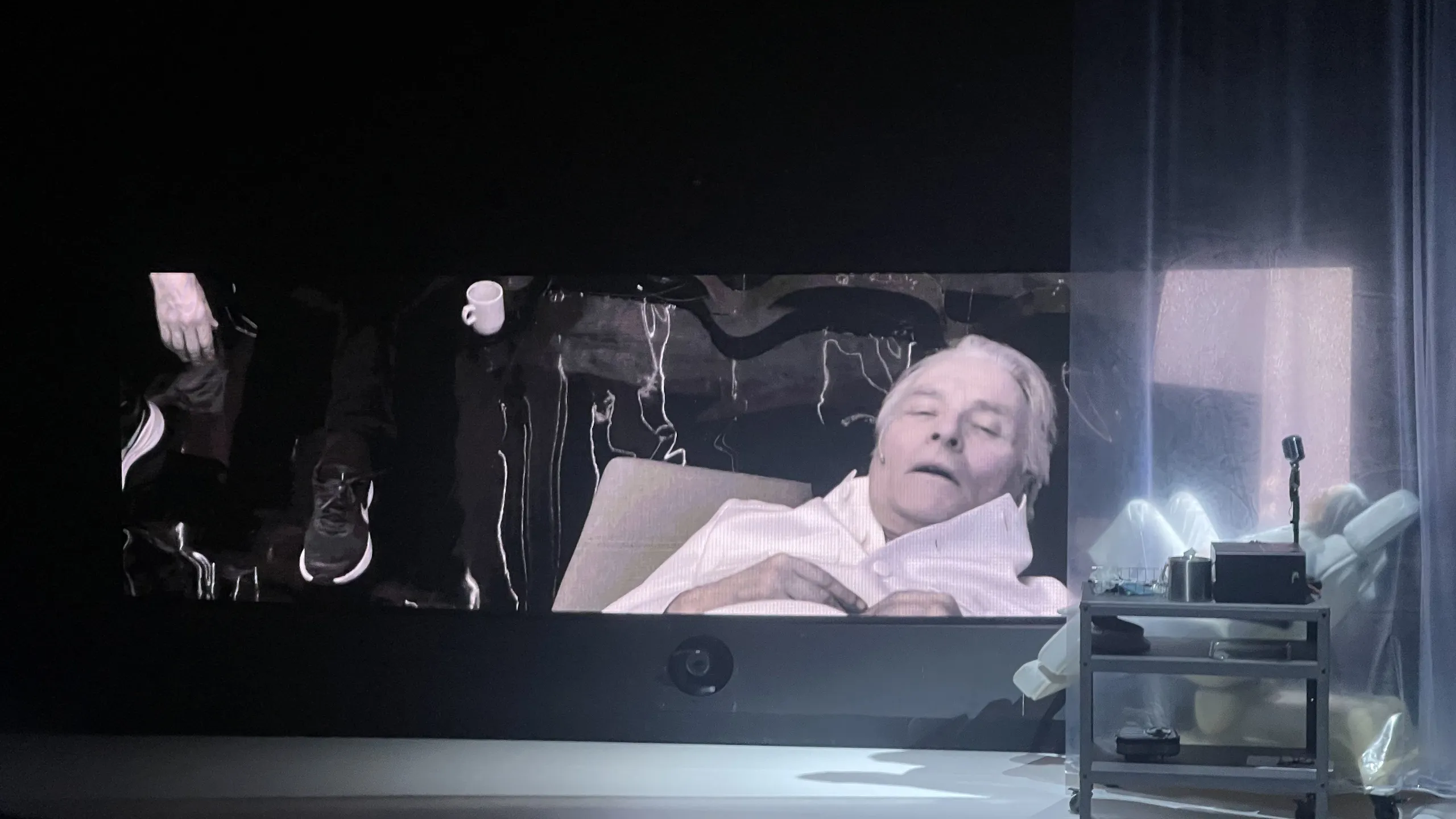 Prøvebilder fra scenen til forestillingen Kallocain - vi ser en mann som ligger i en tannlegelignende stol. Vi ser fjeset hans på en stor skjerm bak.