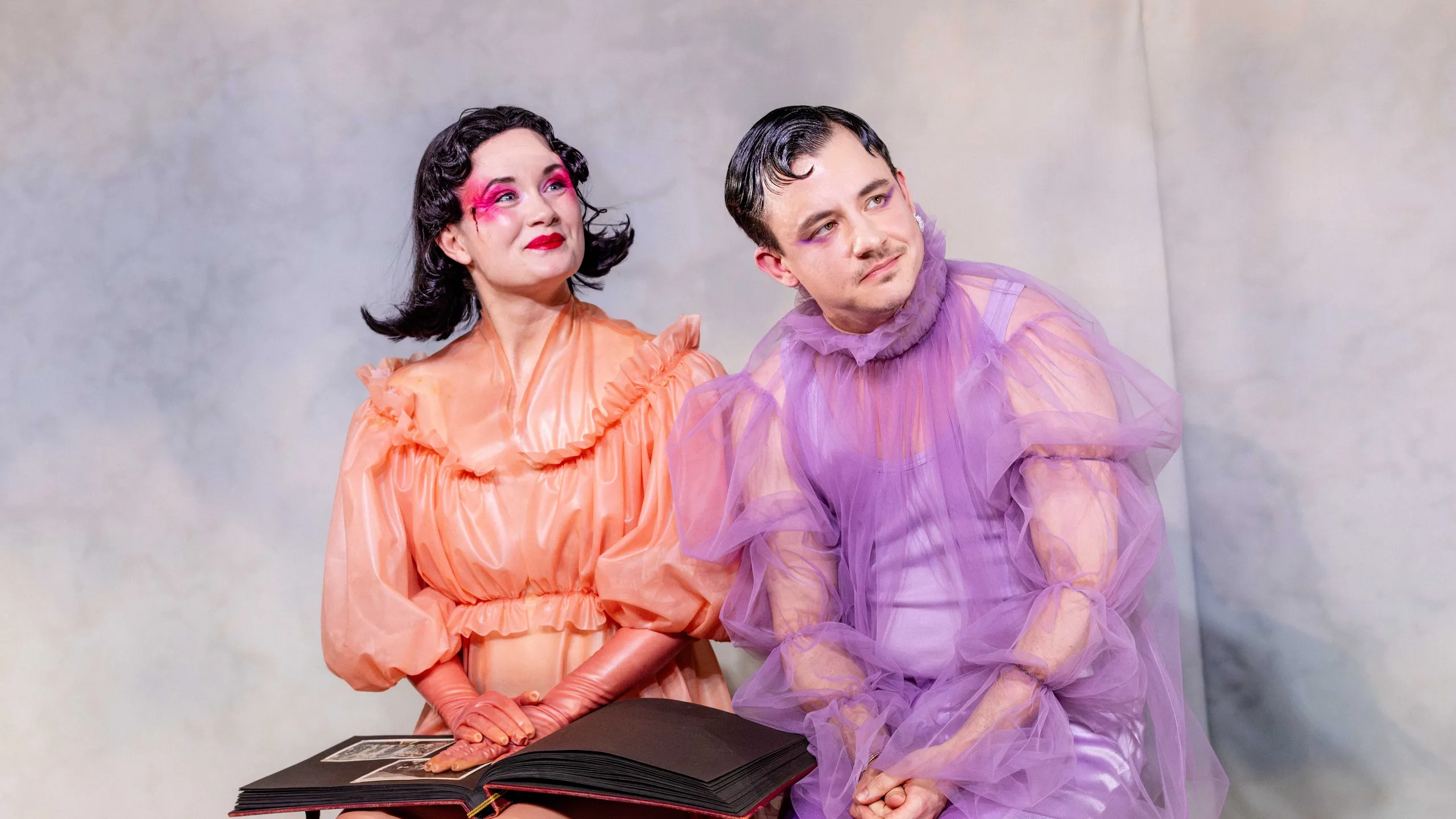 To personer sitter sammen på en benk og ser opp mens en stor fotoalbum ligger åpent i fanget