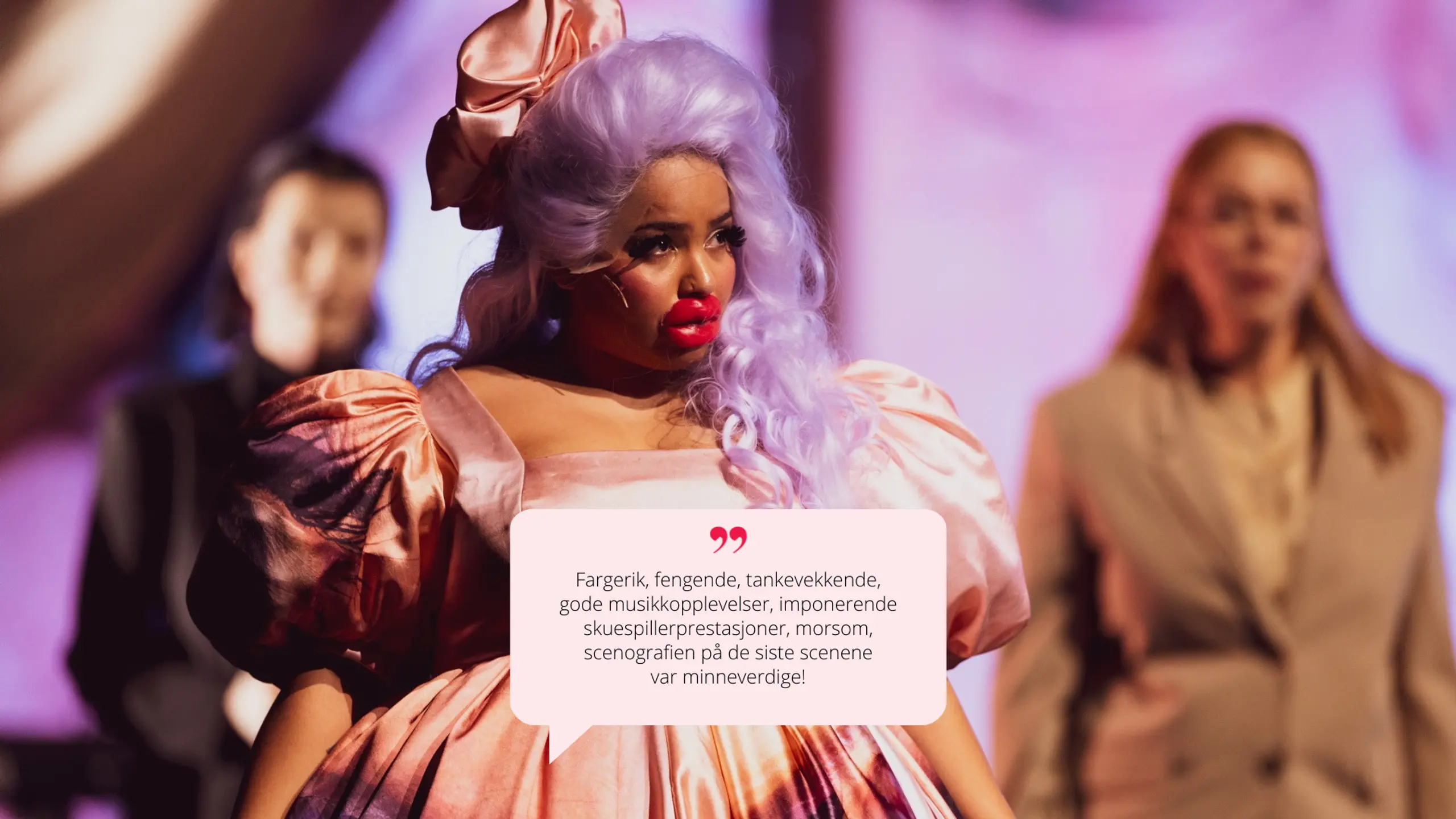 En karakter med dramatisk sminke, lys lilla parykk og voluminøs, barokk-inspirert kjole i rosa og oransje nyanser. Scenen er fargerik og teatralsk.  🗨️ Sitat i snakkeboble:  "Fargerik, fengende, tankevekkende [...] scenografien på de siste scenene var minneverdige!"