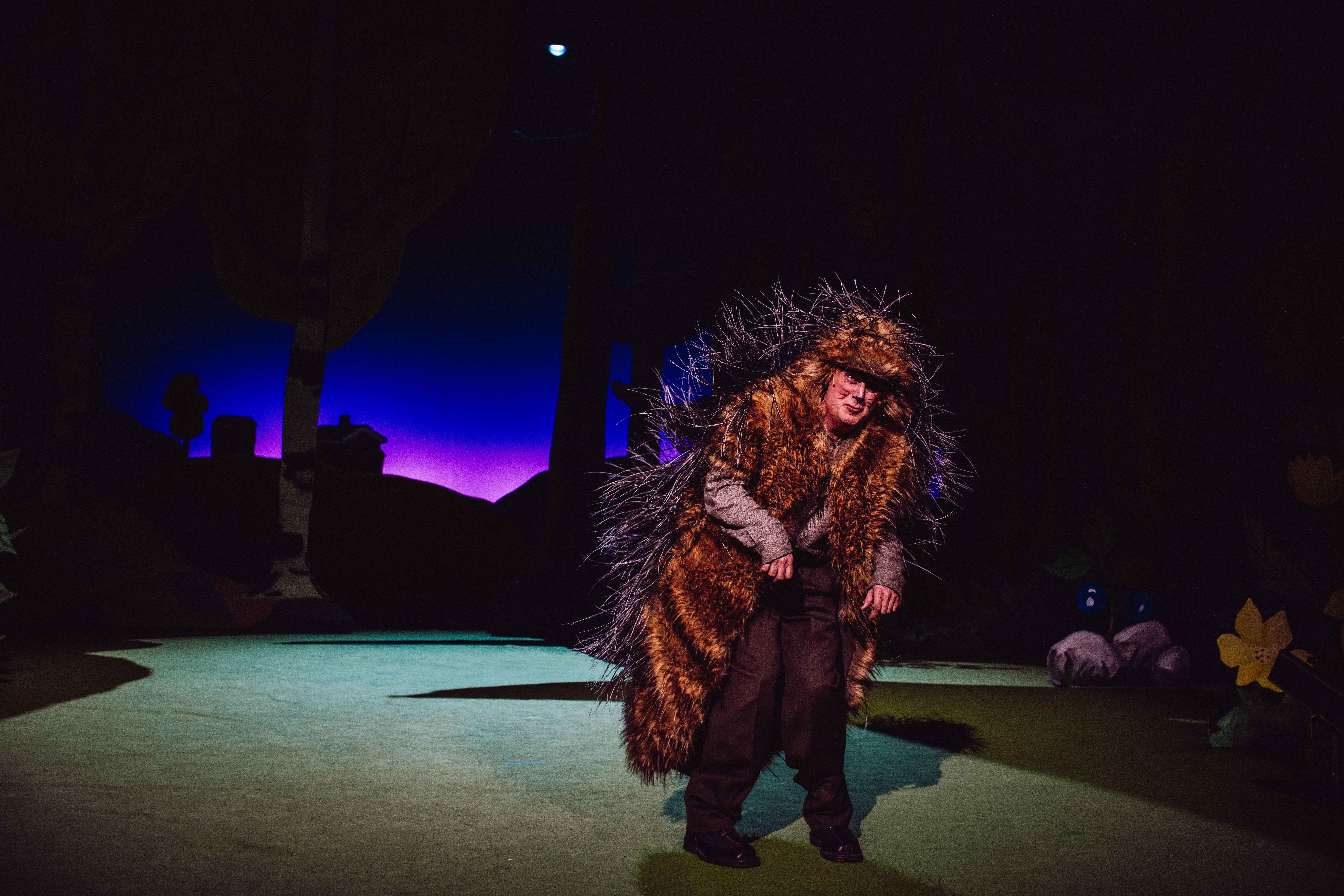 En karakter utkledd som pinnsvin bøyer seg fremover på en mørklagt scene med lilla baklys.