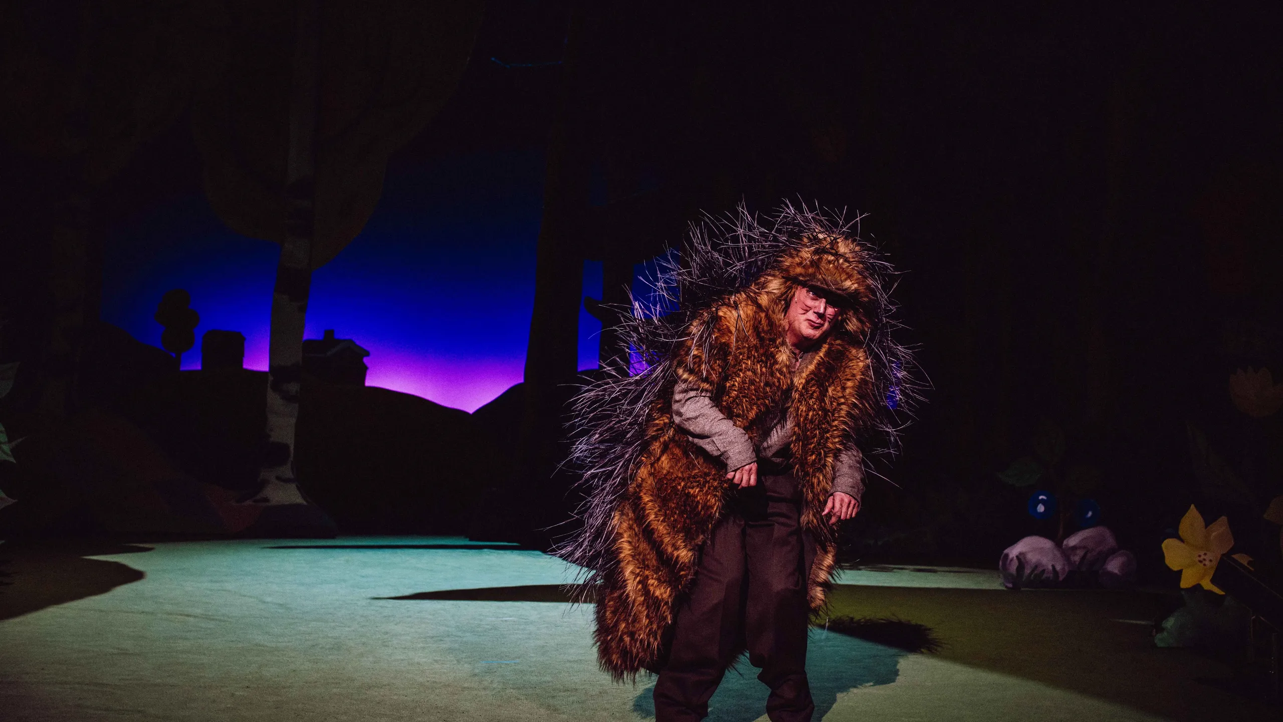 En karakter utkledd som pinnsvin bøyer seg fremover på en mørklagt scene med lilla baklys.