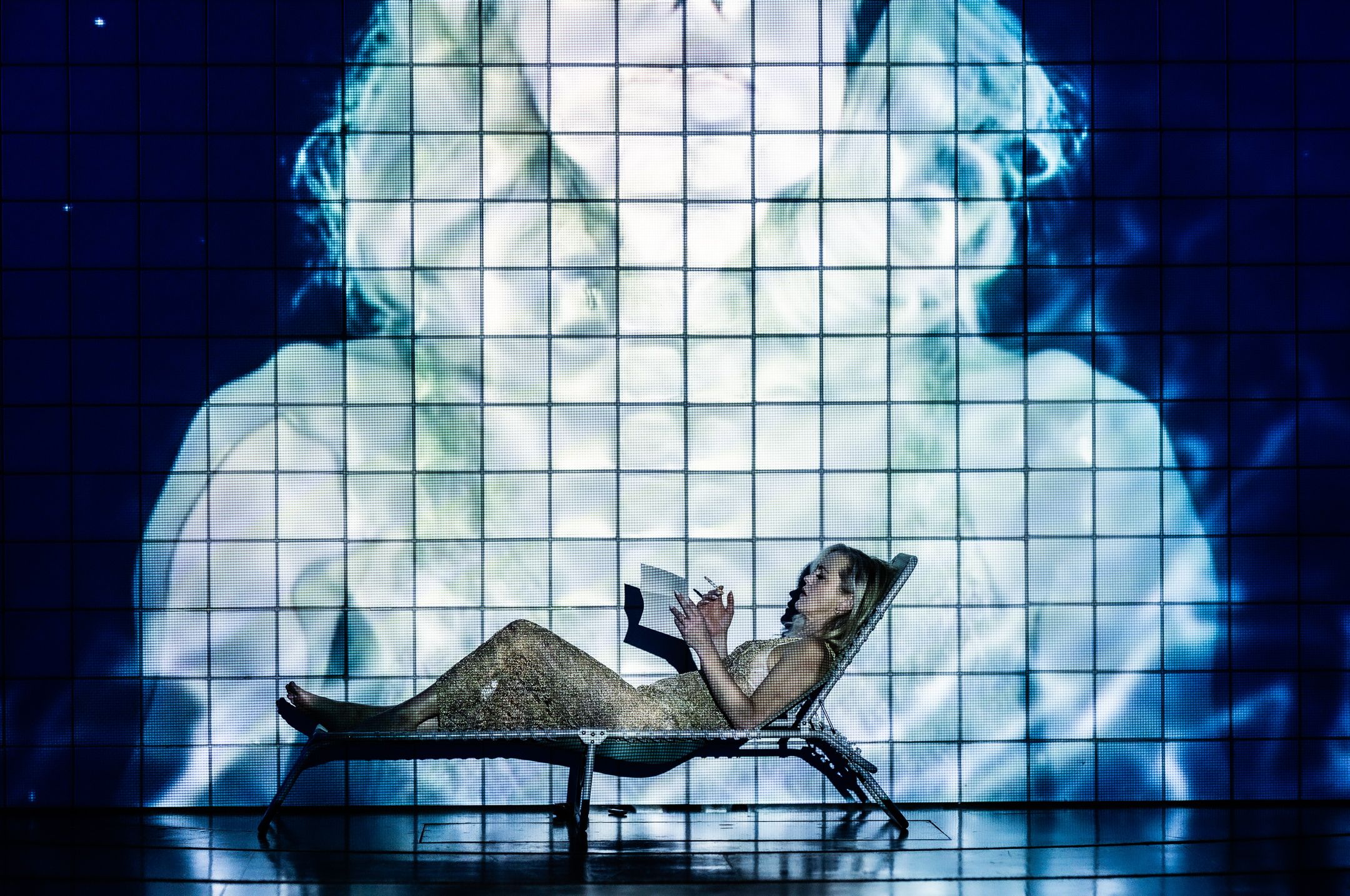 Kvinne ligger i solseng og røyker og leser brev med projeksjon på veggen bak