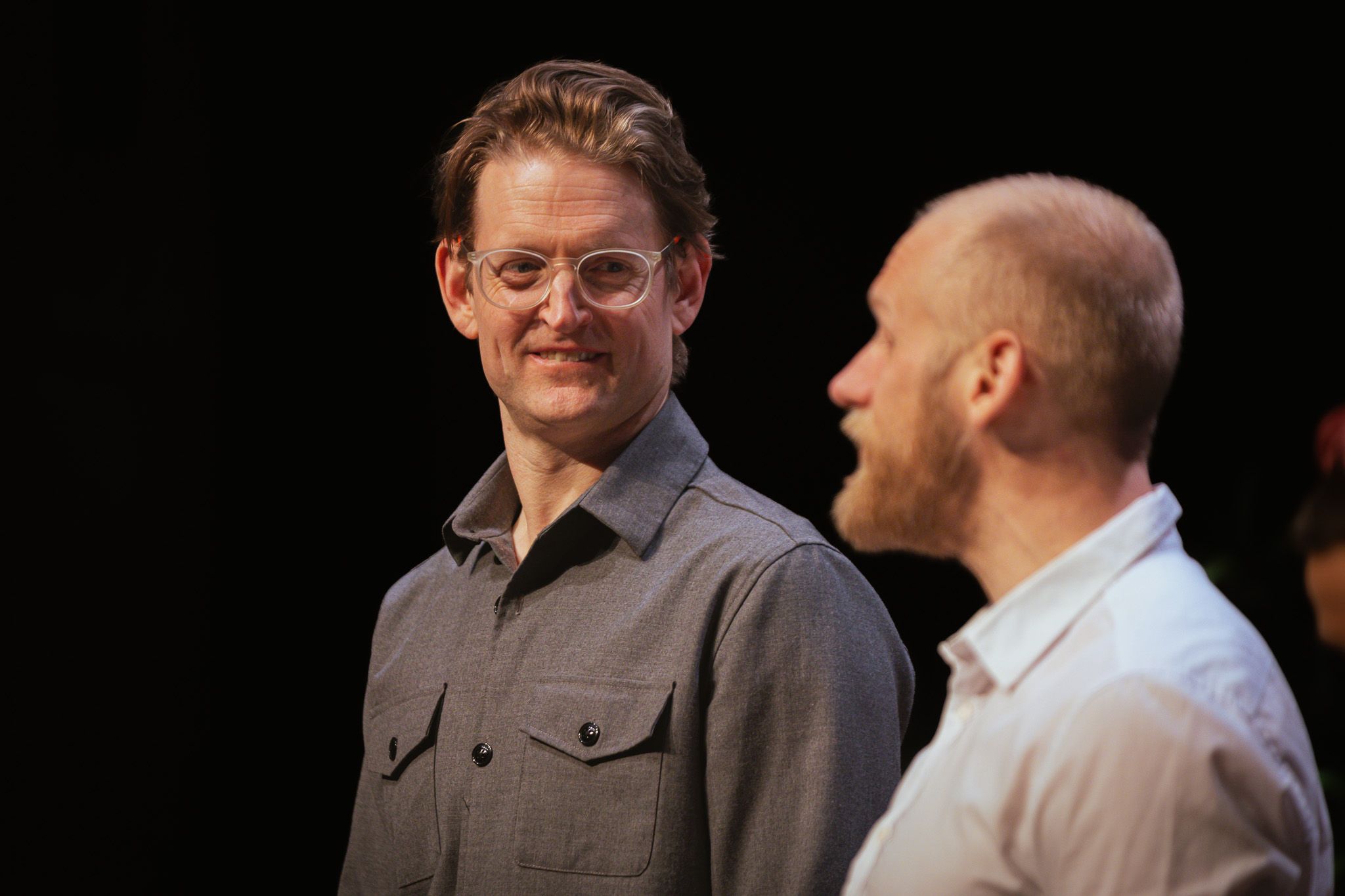 To personer i samtale, én med briller smiler mens den andre snakker i profil