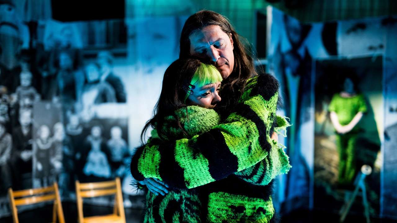 Mann og kvinne i neongrønne kostymer i tett klem. Hun gråter.
