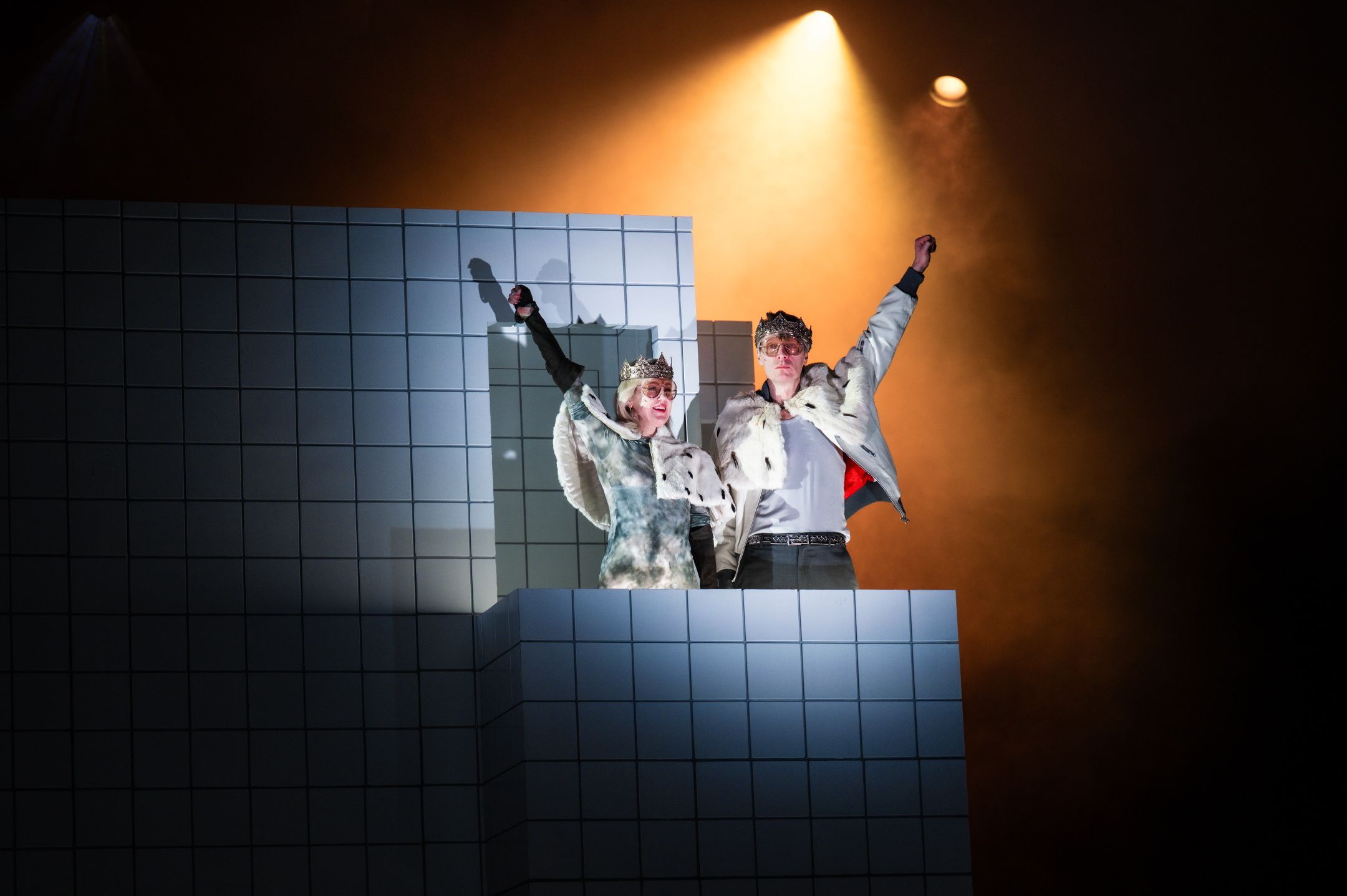 Mann og kvinne kledd som kongelige står med hendene opp på flislagt balkong