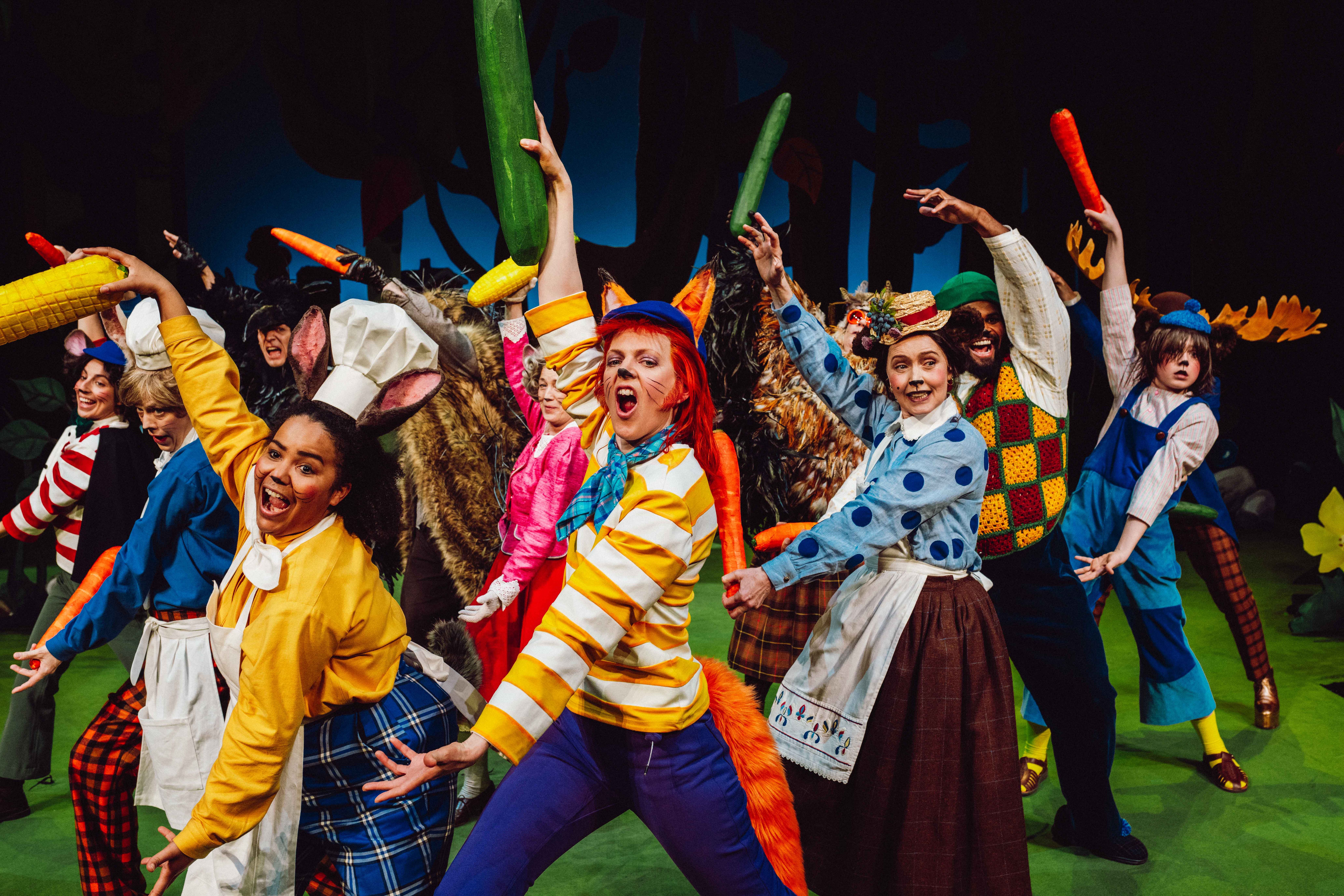 En gruppe kostymekledde karakterer danser med store grønnsaker på en grønn scene.
