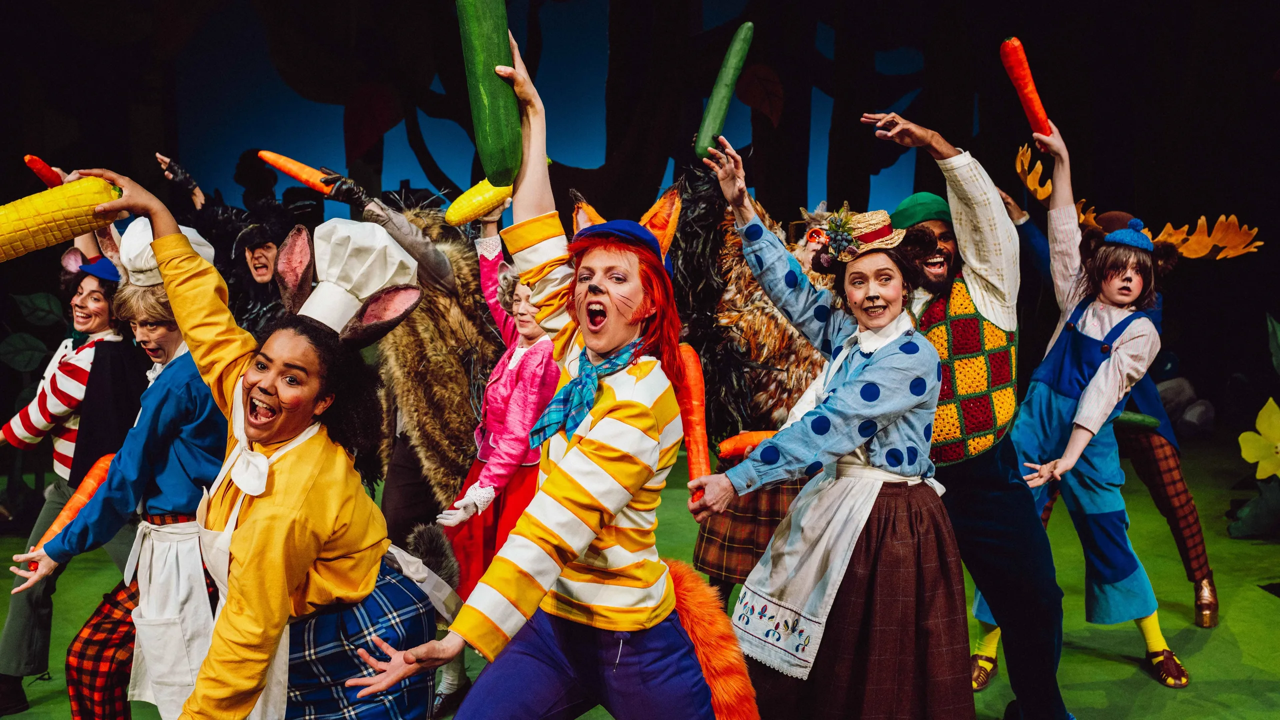 En gruppe kostymekledde karakterer danser med store grønnsaker på en grønn scene.