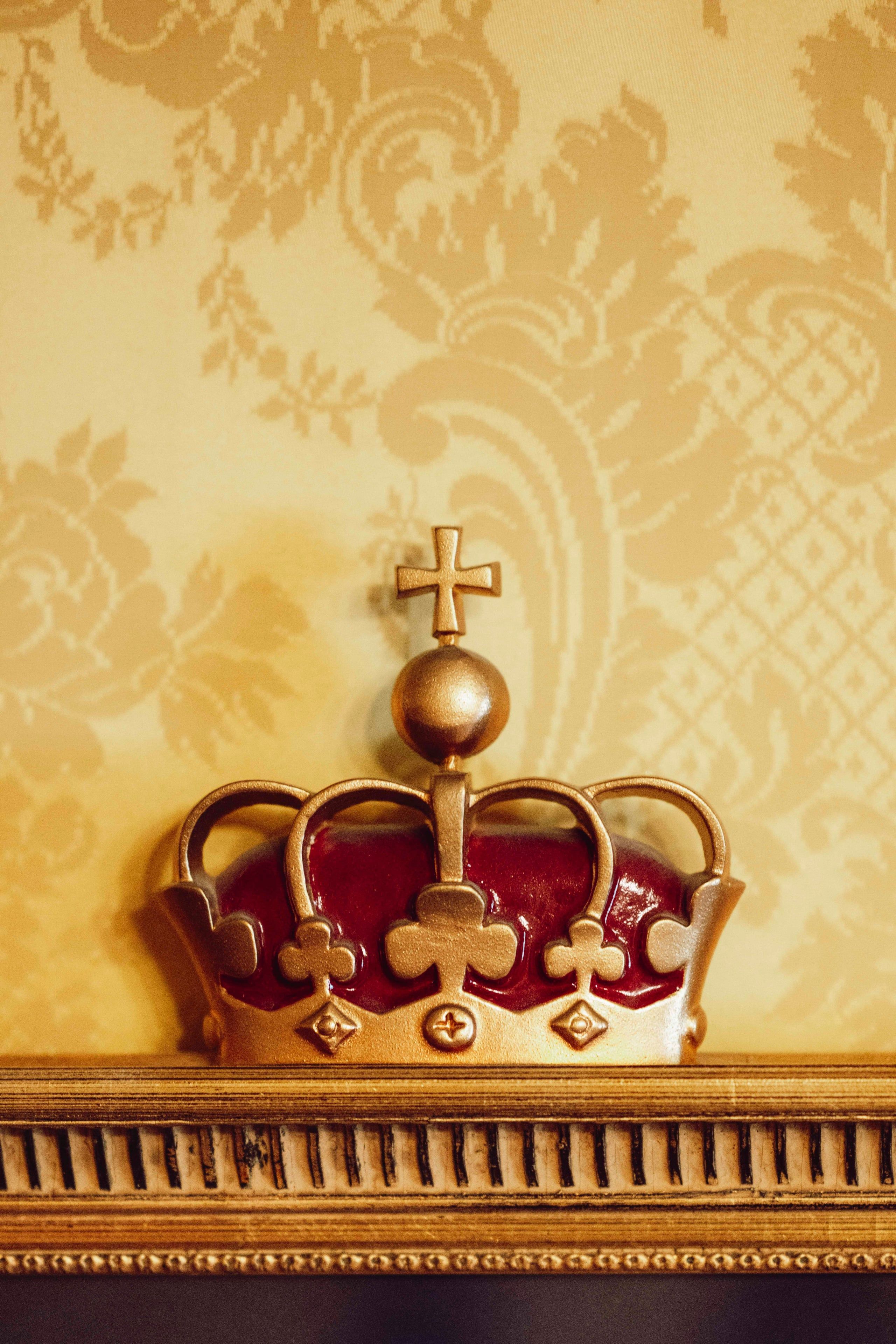 Nærbilde av kroneornament i Kongelosjen med forgylte detaljer og mønstret veggtekstil i bakgrunnen.