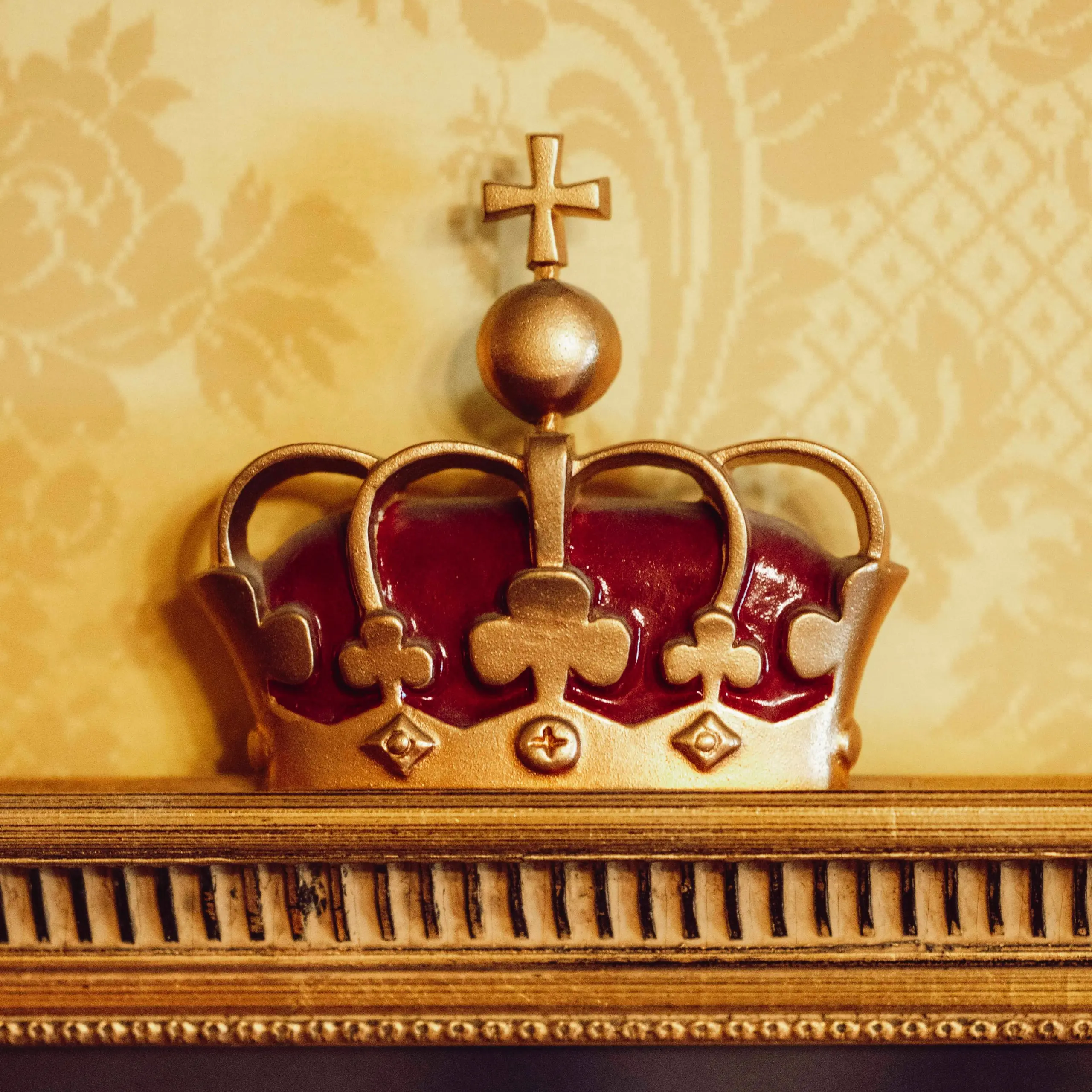 Nærbilde av kroneornament i Kongelosjen med forgylte detaljer og mønstret veggtekstil i bakgrunnen.