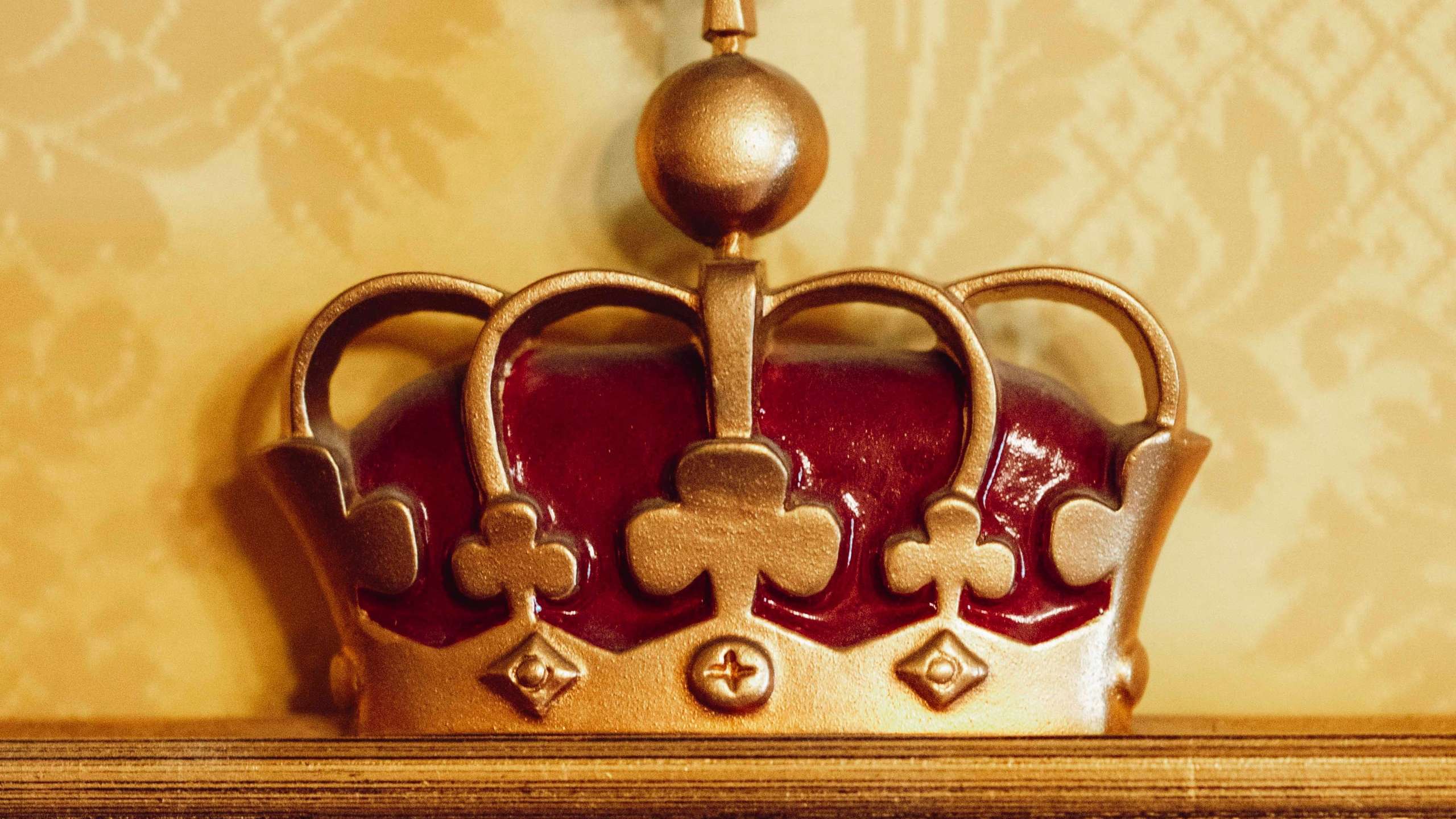 Nærbilde av kroneornament i Kongelosjen med forgylte detaljer og mønstret veggtekstil i bakgrunnen.