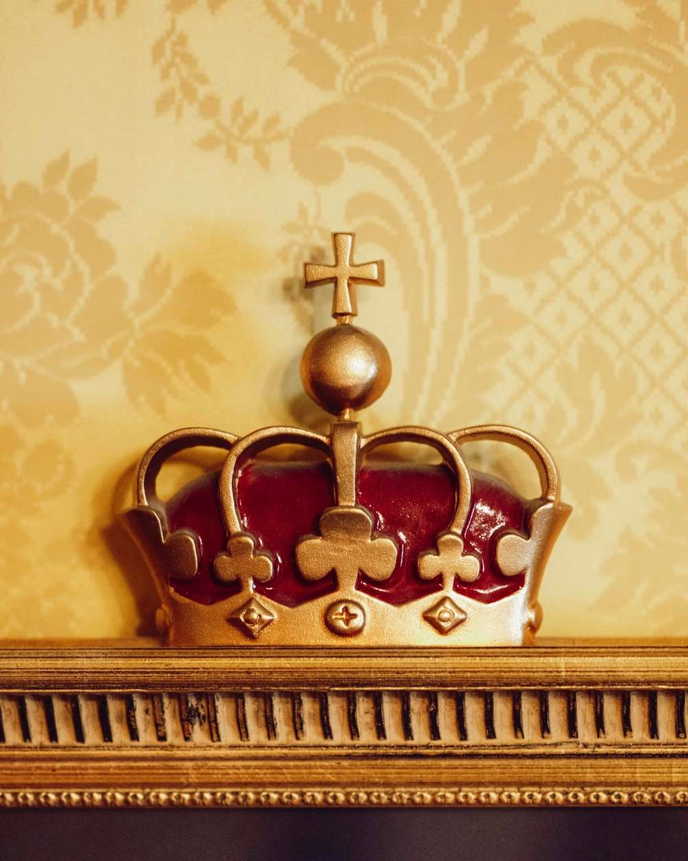 Nærbilde av kroneornament i Kongelosjen med forgylte detaljer og mønstret veggtekstil i bakgrunnen.