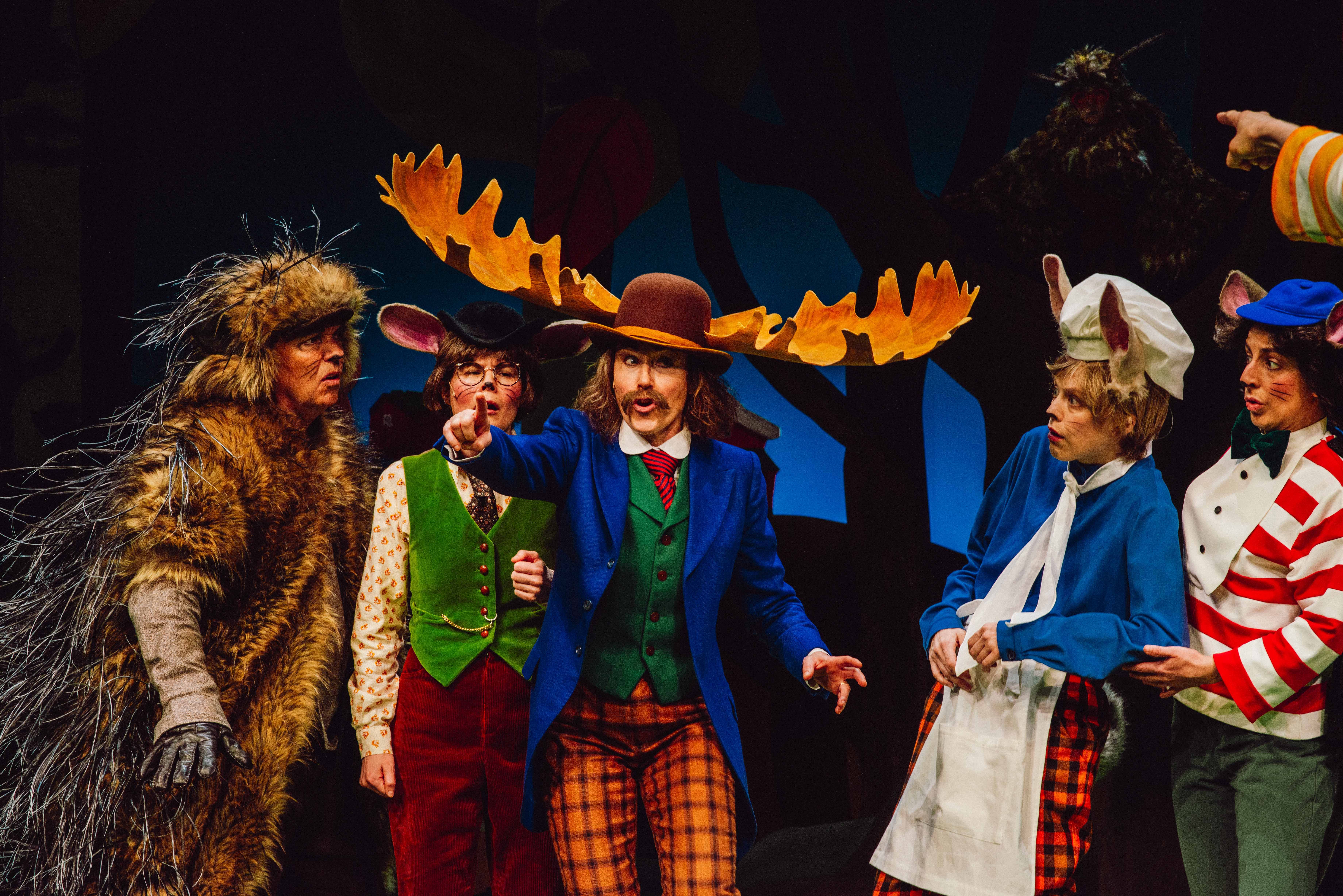 Gruppe karakterer, inkludert en elg med store gevir og mus med kokkelue, samles i diskusjon.