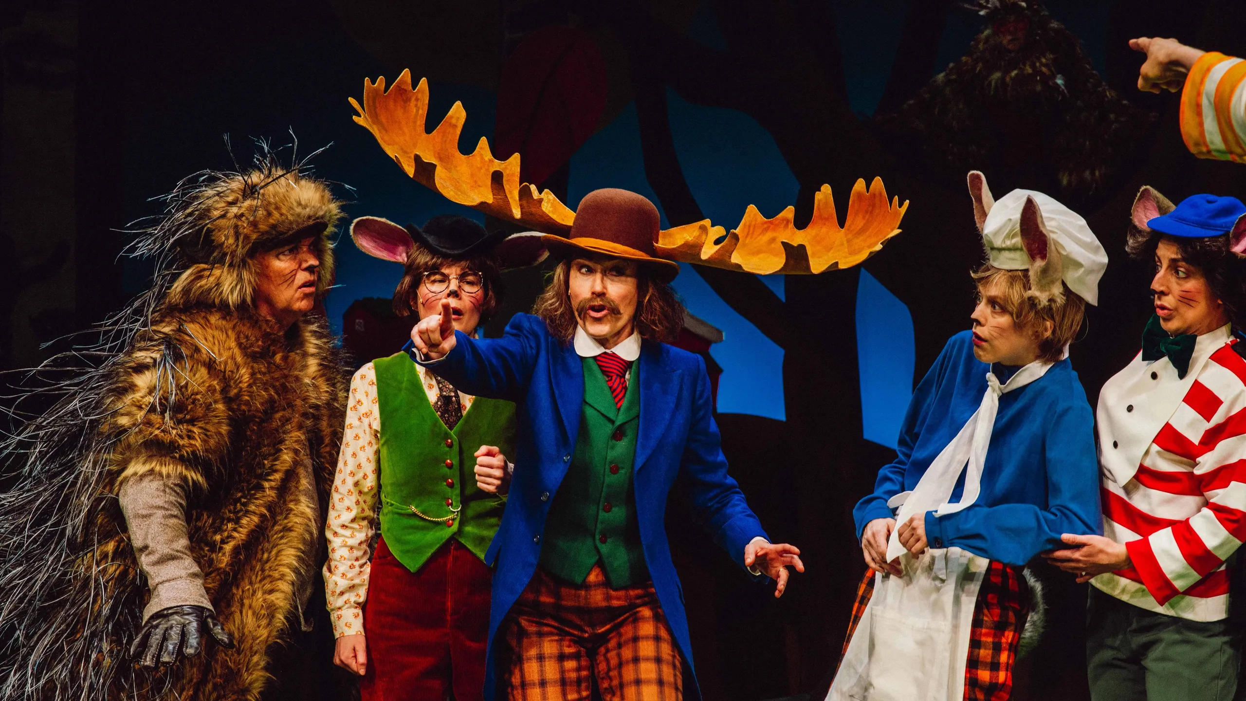 Gruppe karakterer, inkludert en elg med store gevir og mus med kokkelue, samles i diskusjon.