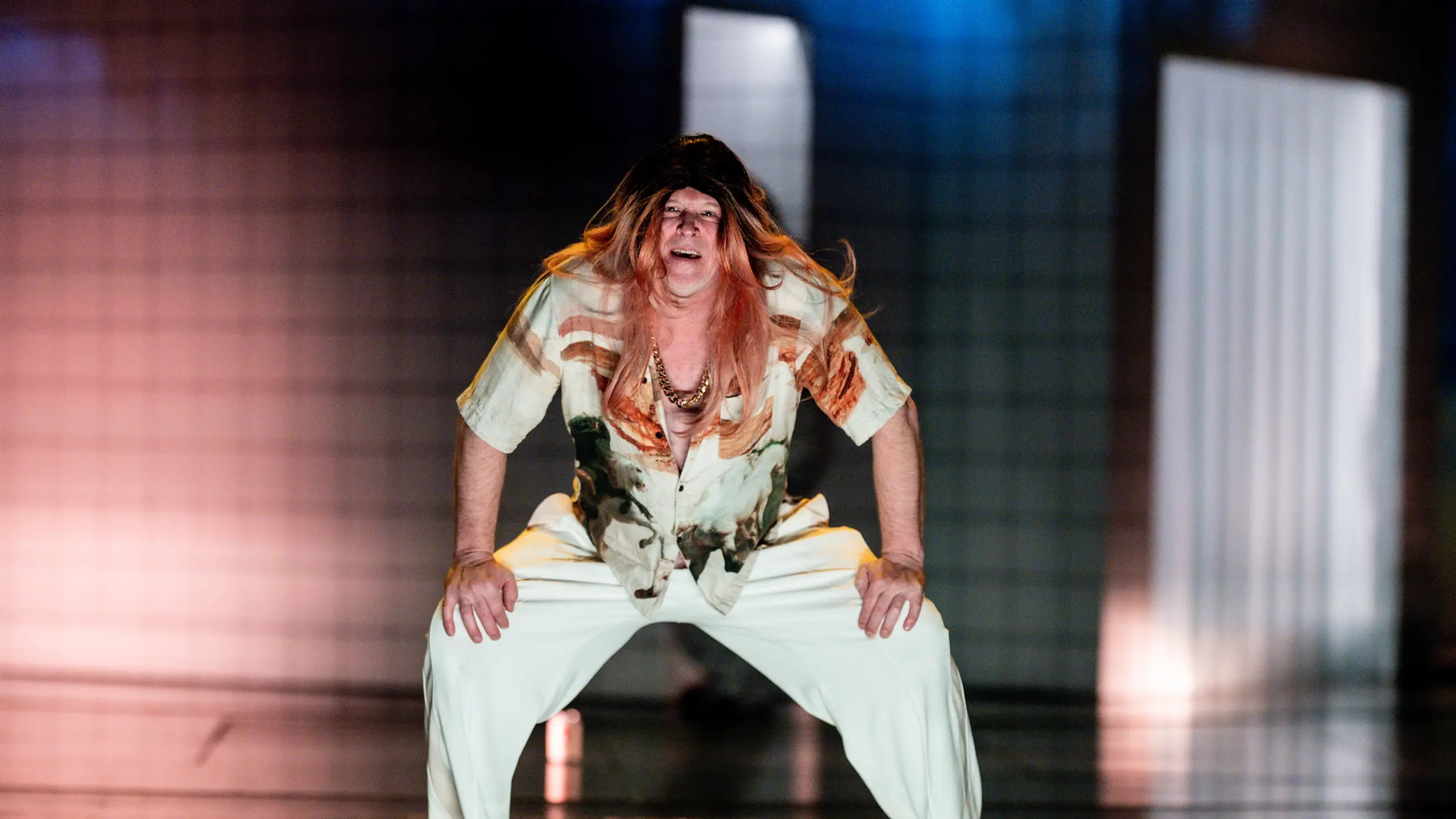 Mann med langt hår smiler og holder seg på knærne på en scene