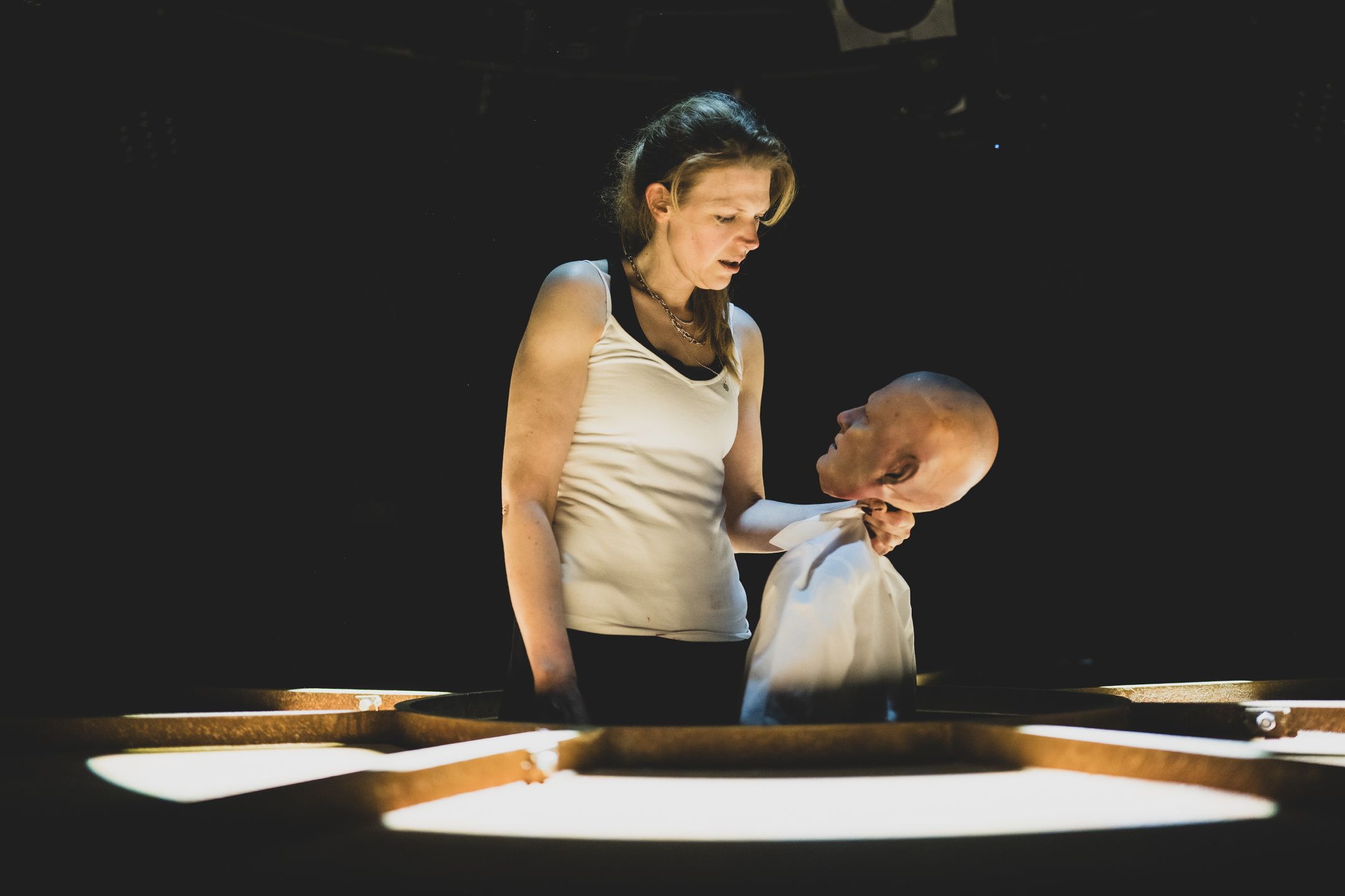 Kvinne holder dukke i skjortekrage og stirrer alvorlig på den i mørklagt rom