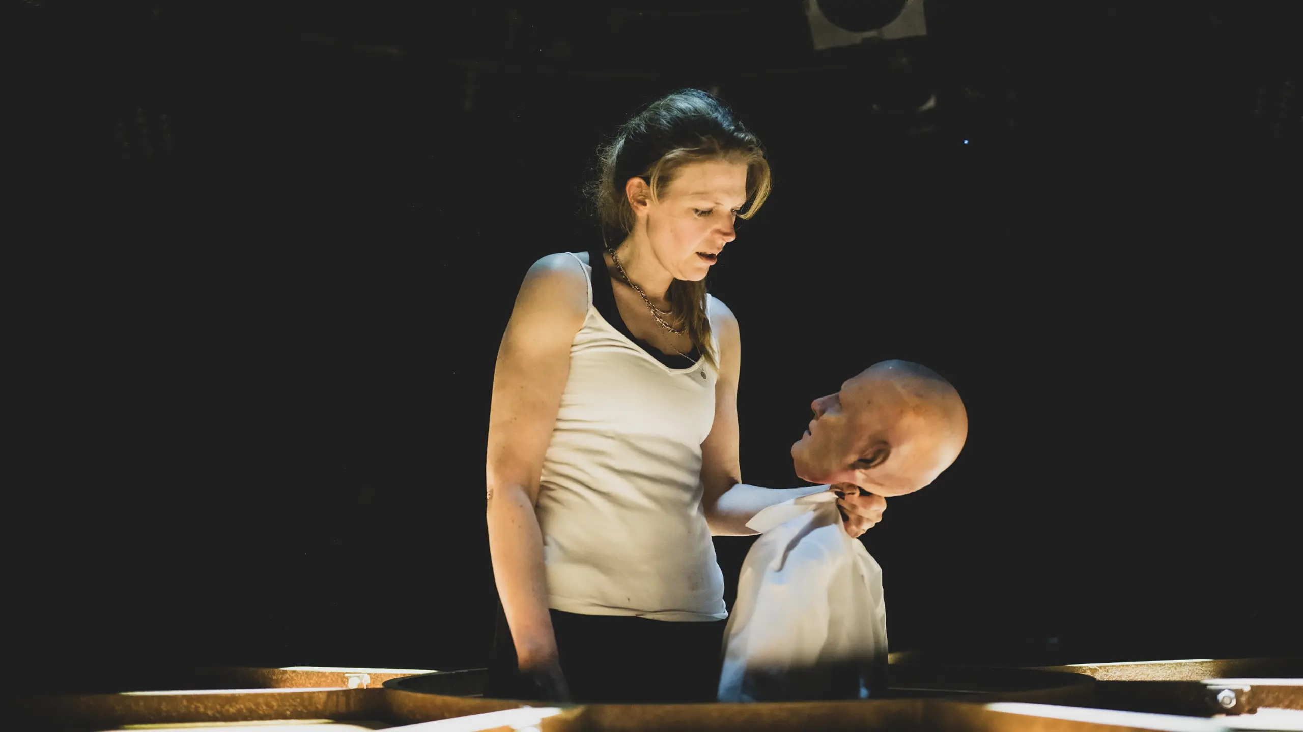 Kvinne holder dukke i skjortekrage og stirrer alvorlig på den i mørklagt rom