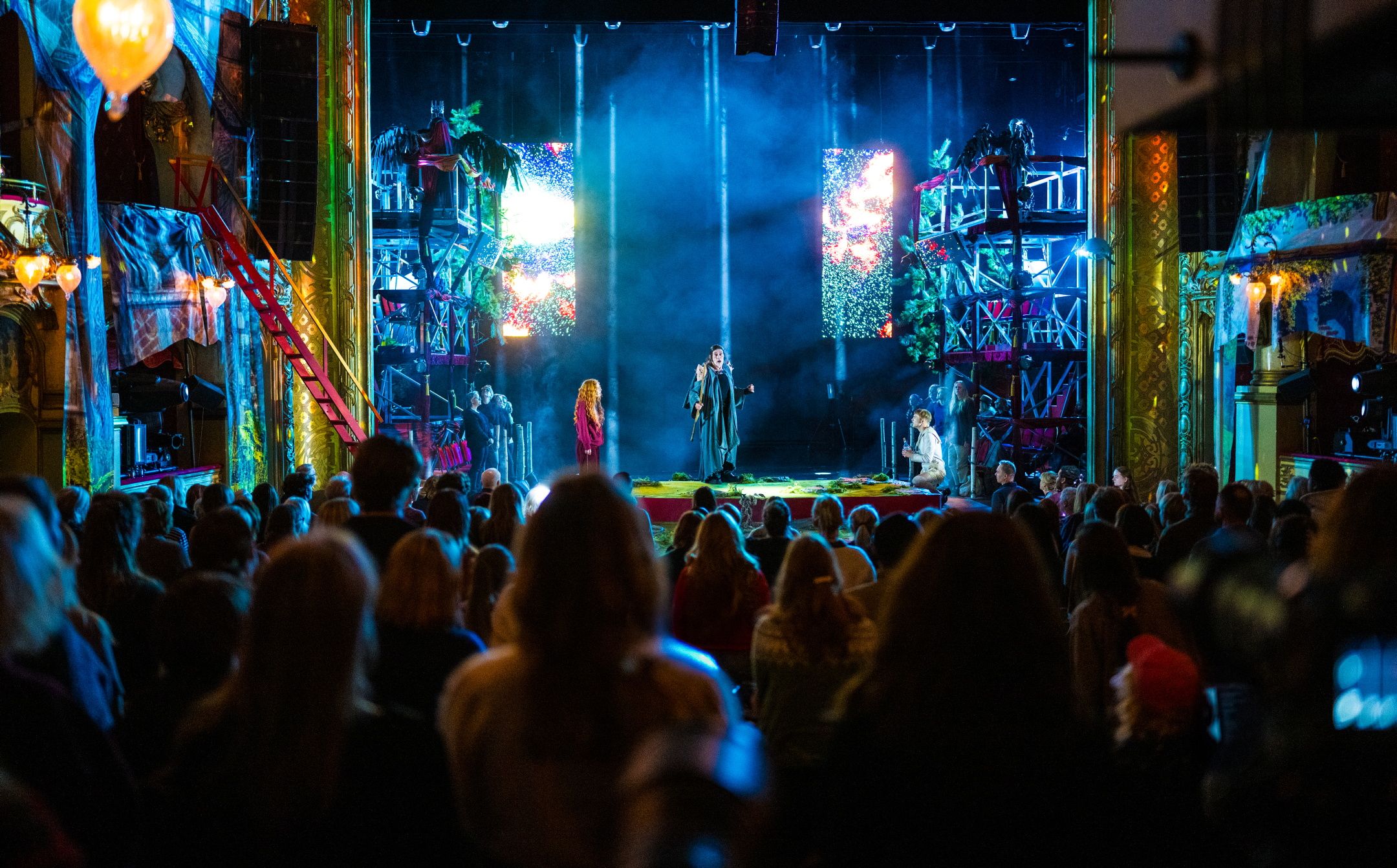 Fullsatt hovedscene med publikum, masse lys og stillas og noen skuespillere på scenen