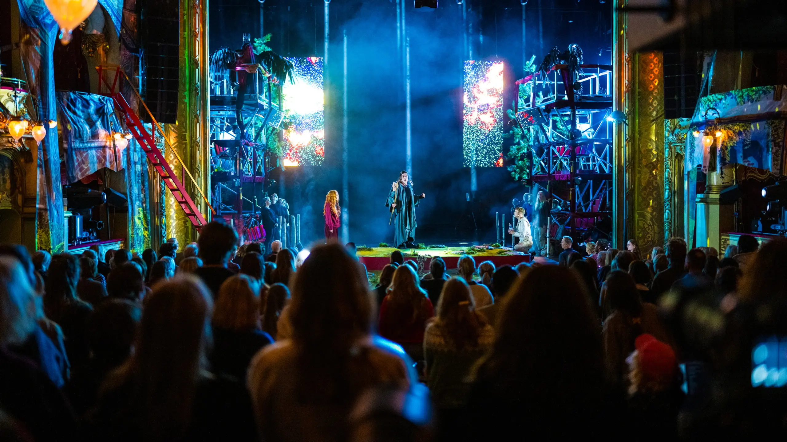 Fullsatt hovedscene med publikum, masse lys og stillas og noen skuespillere på scenen
